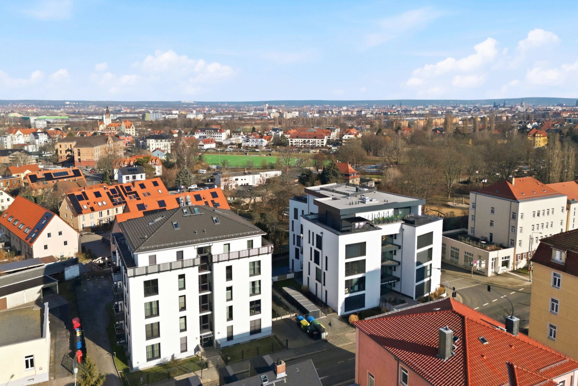Vogelperspektive auf moderne Wohngebäude und umliegende Stadtlandschaft bei klarem Himmel.