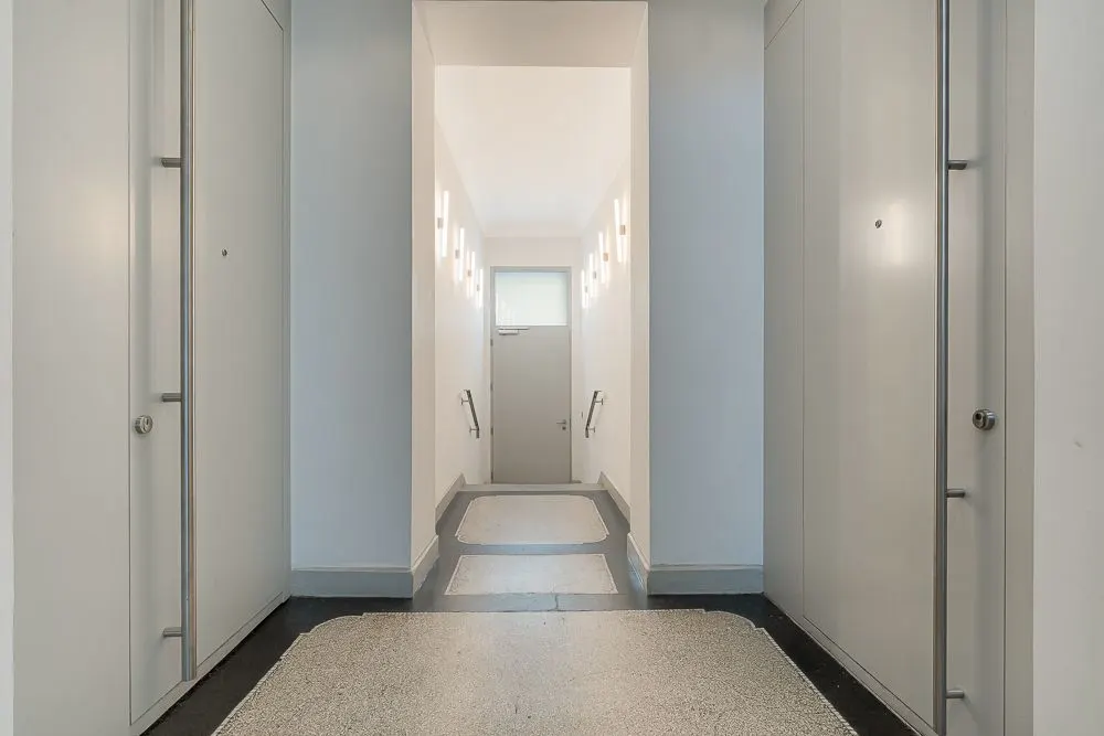 Heller Flur mit Türen und einem Fenster am Ende, Handläufe an den Wänden.