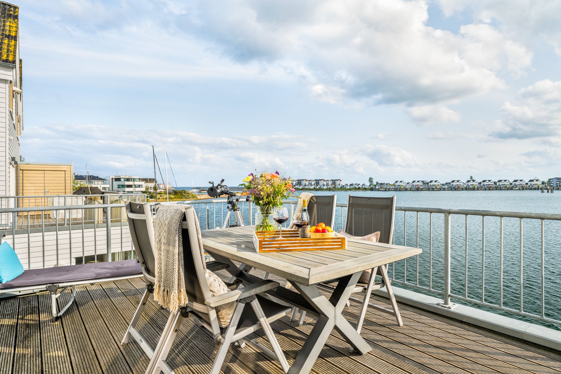 Holzbalkon mit Tisch, Stühlen und Blick auf das Wasser.