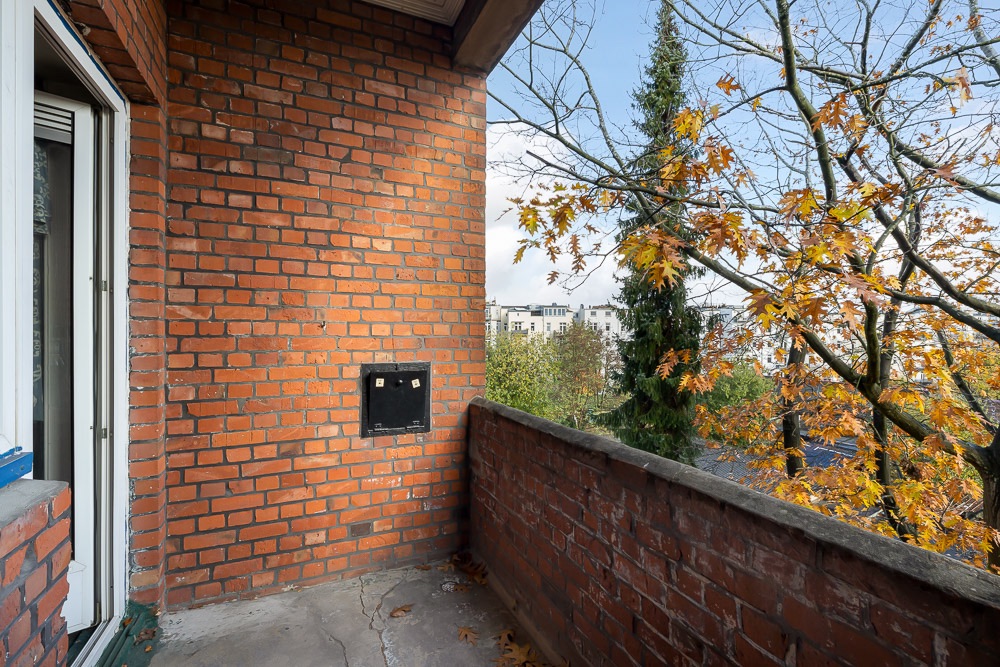 Balkon mit Backsteinwänden, Ausblick auf Bäume mit Herbstlaub und Gebäude im Hintergrund.