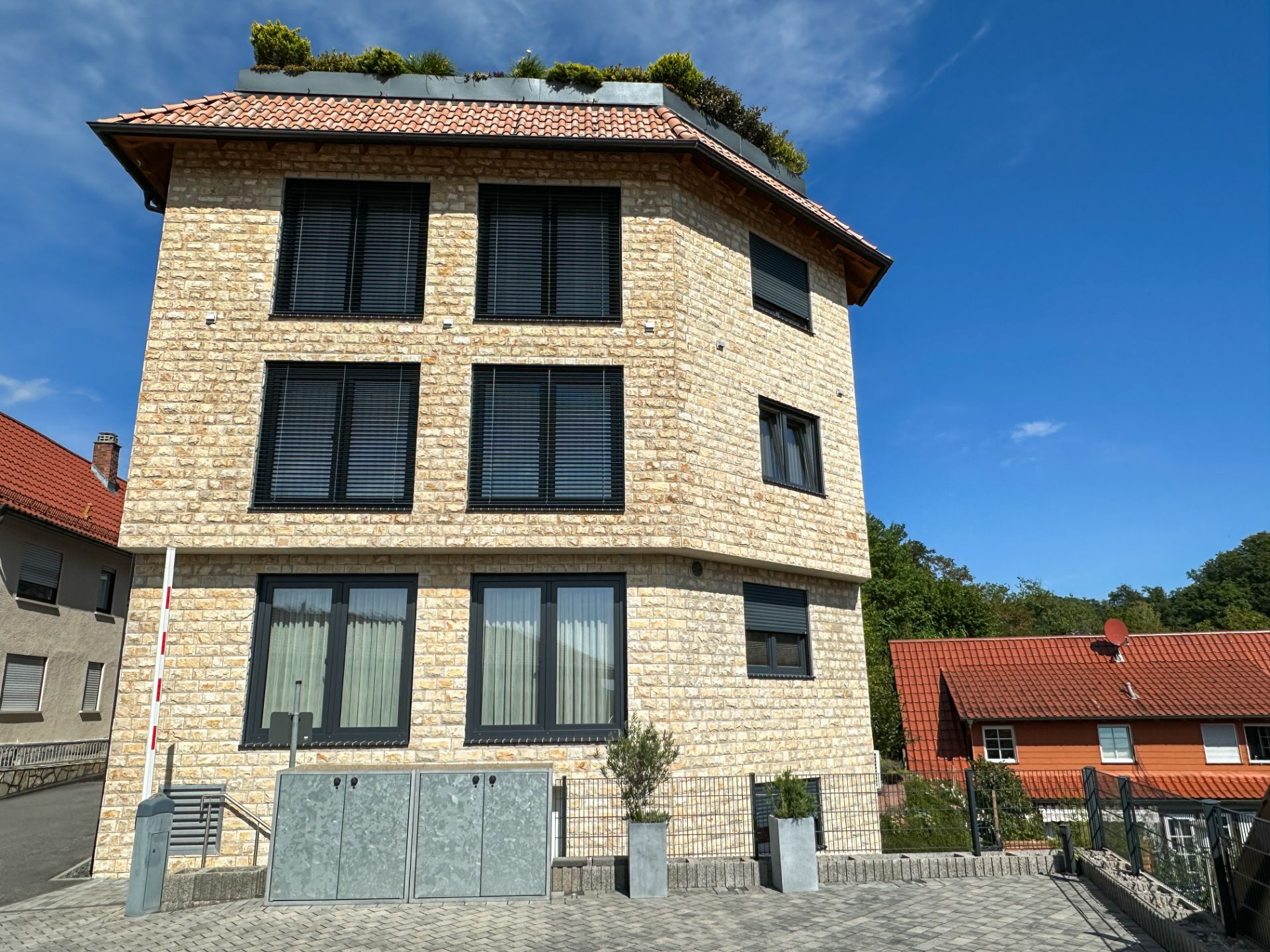 Modernes Wohnhaus mit gelber Ziegelfassade, großen Fenstern und rotem Dach bei Sonnenschein.