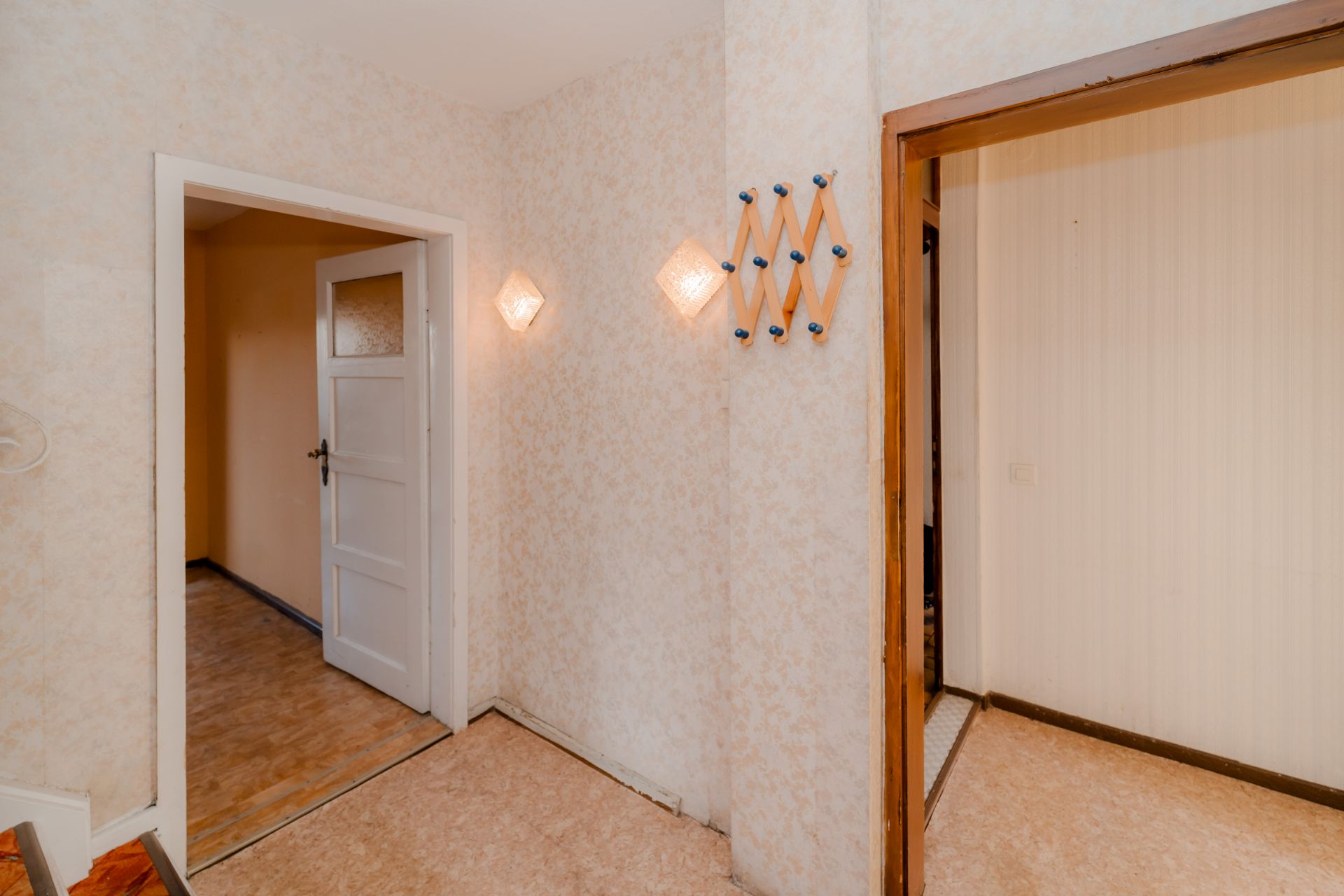 Heller Flur mit offener Tür, Wandhaken und zwei Wandleuchten.