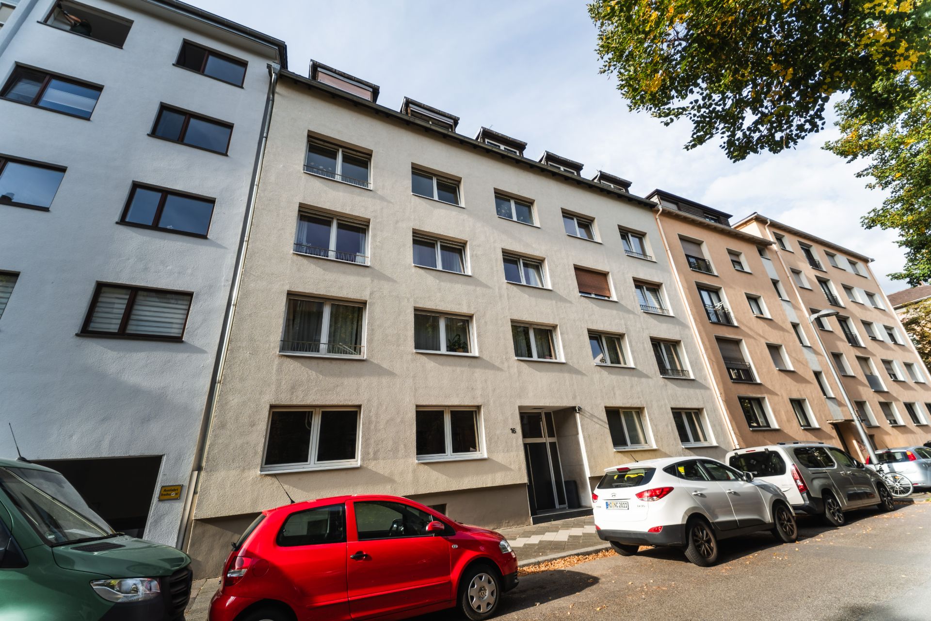 Mehrstöckiges Wohnhaus mit mehreren Autos, die an der Straße davor parken.