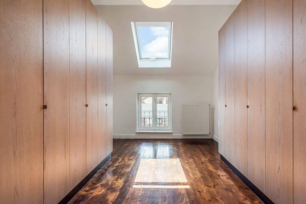 Flur mit Holzboden, zwei Reihen Holzschränken, Dachfenster und Fenster mit Heizkörper.
