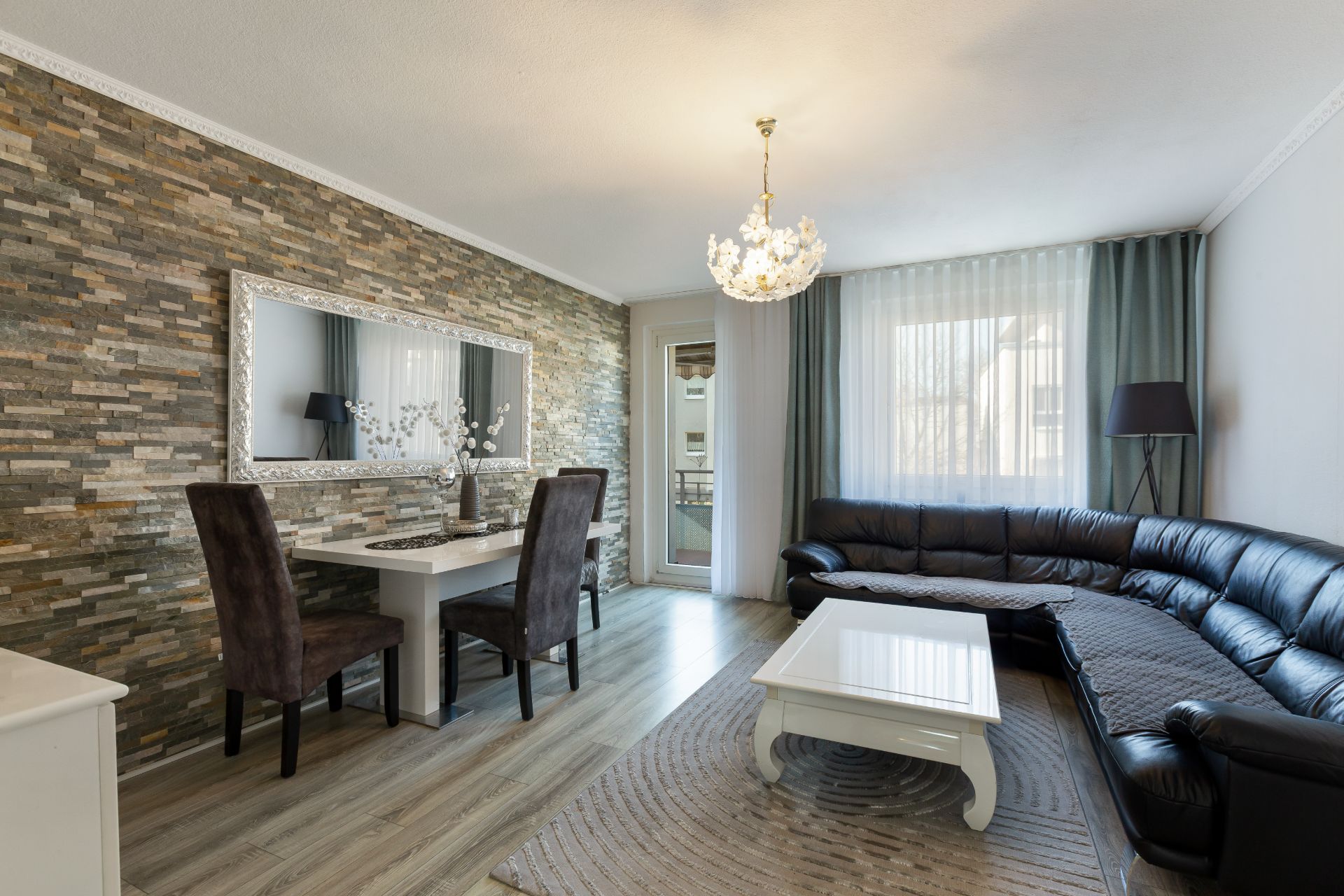 Modernes Wohnzimmer mit Ecksofa, Esstisch, Spiegel und Stehlampe vor Steinwand.