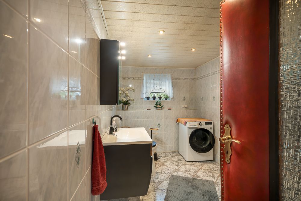 Modernes Badezimmer mit Waschbecken, Spiegel, Waschmaschine und Fenster mit Vorhang.