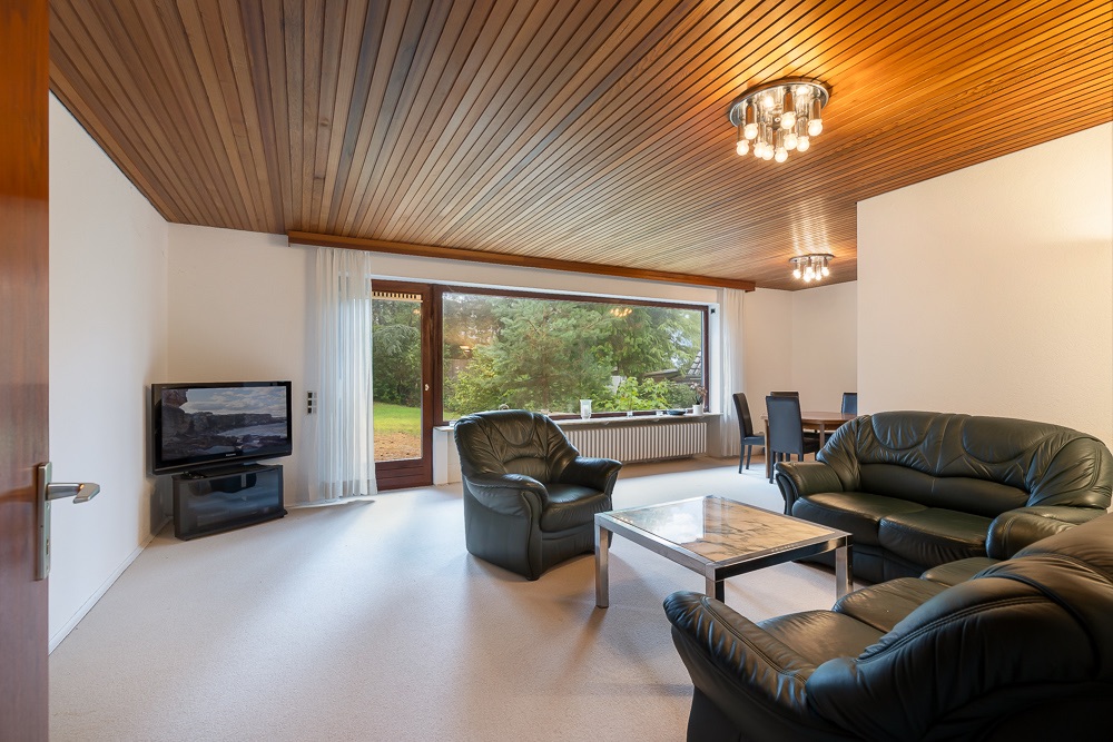 Wohnzimmer mit Ledersofas, Couchtisch, Fernseher und großem Fenster mit Blick ins Grüne.