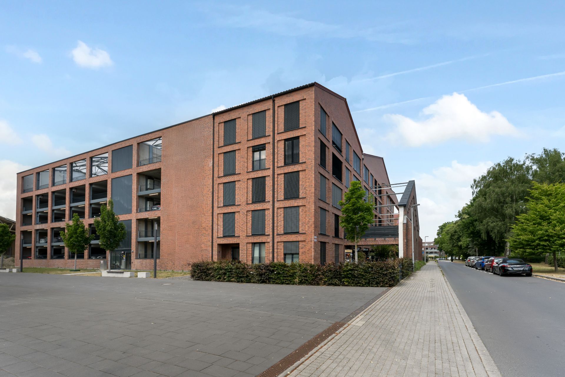 Modernes Wohngebäude aus rotem Backstein an einer ruhigen Straße mit Bäumen.