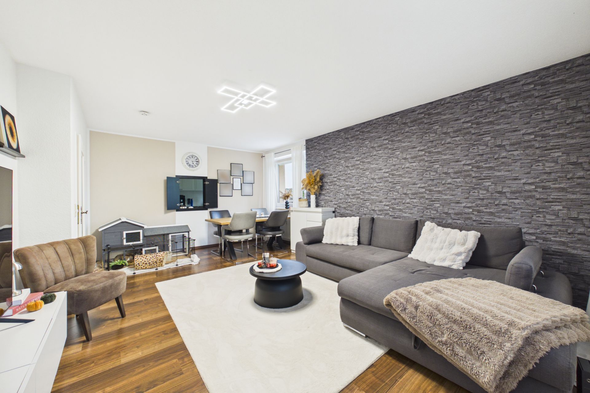 Modernes Wohnzimmer mit grauer Eckcouch, Teppich, kleinem Tisch und Arbeitsplatz an der Wand.