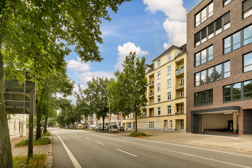 Wohnhäuser und Bäume entlang einer breiten, leeren Straße bei Tageslicht.