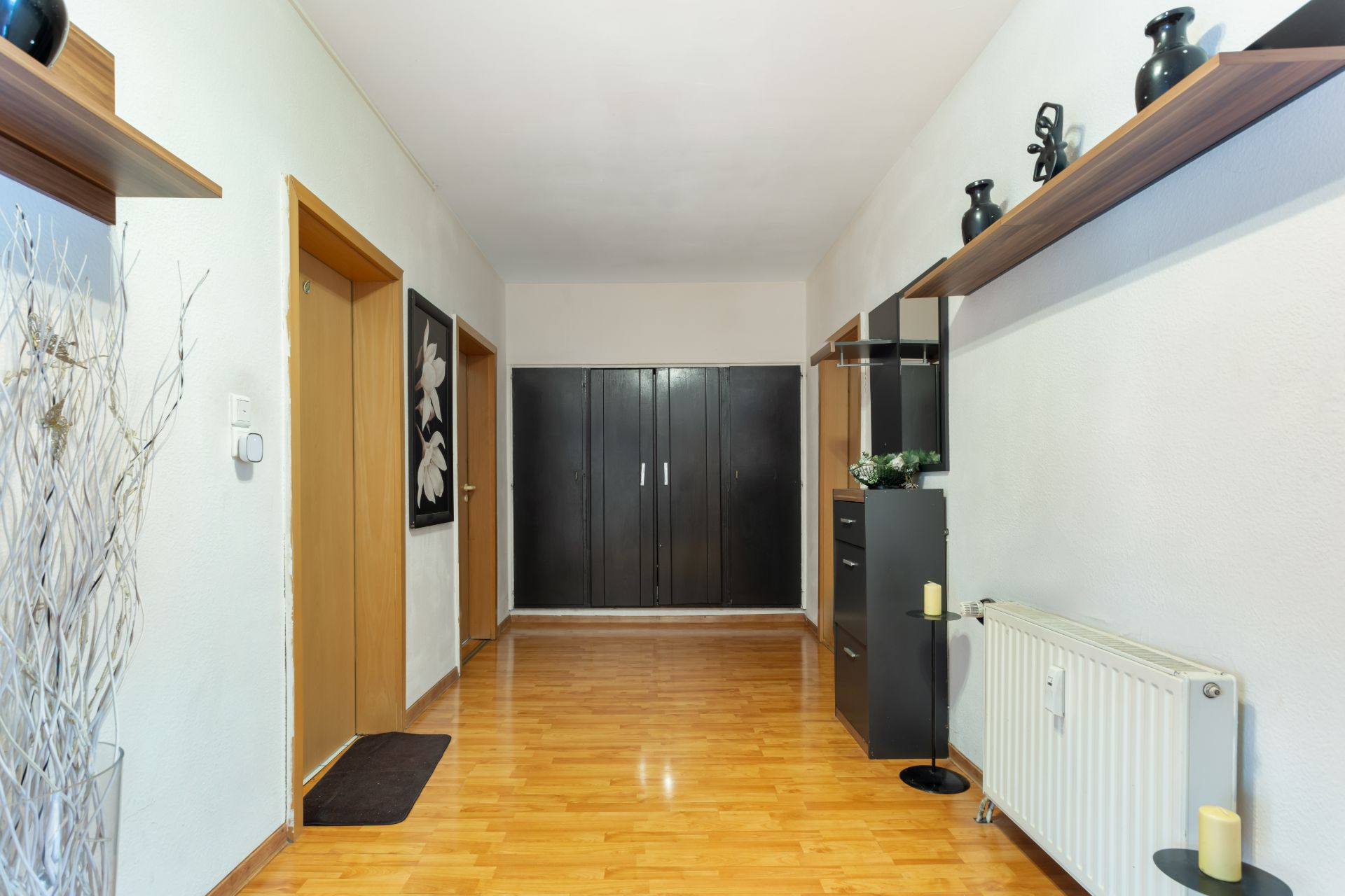Heller Flur mit Holzfußboden, schwarzen Schränken und Dekoration an den Wänden.