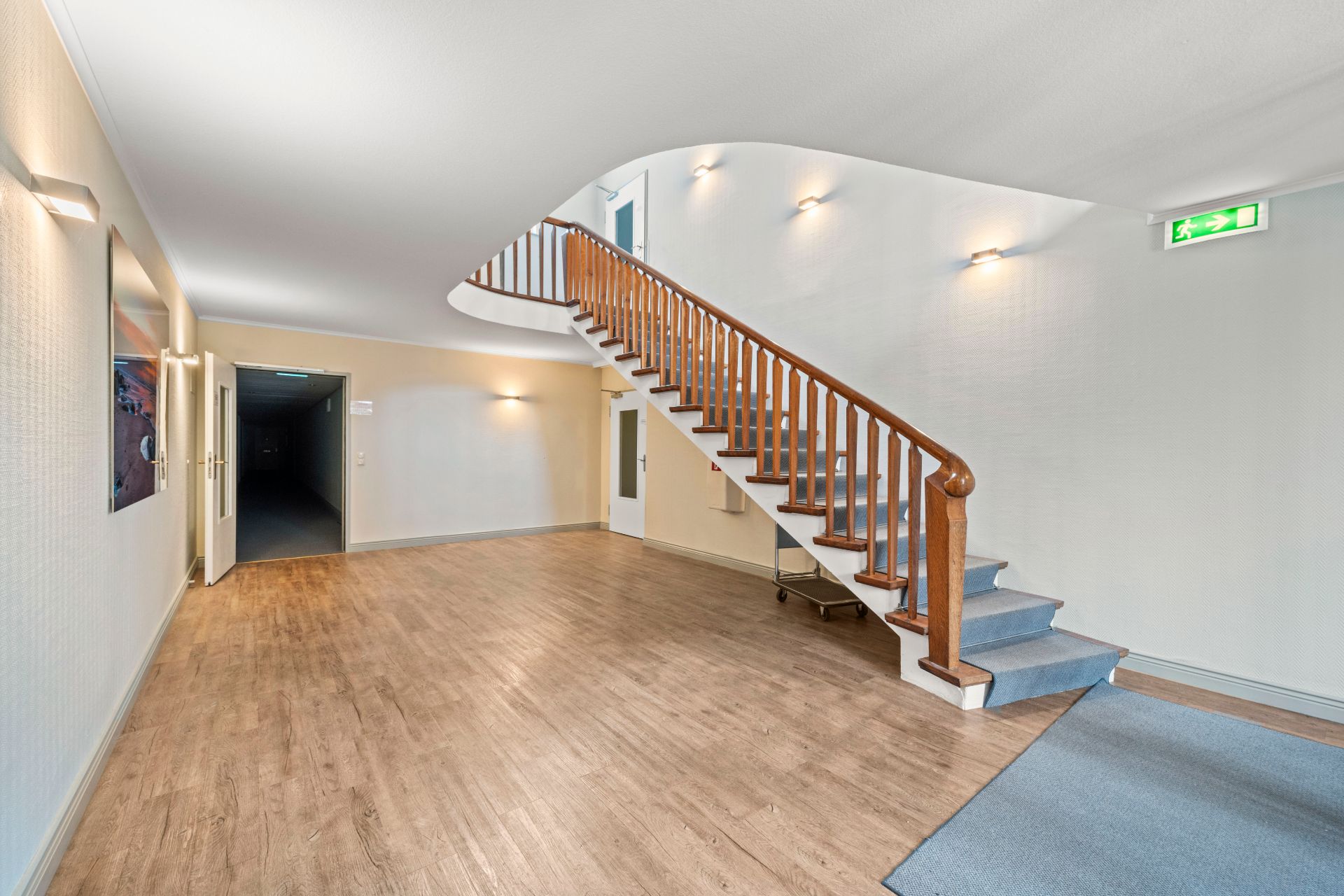 Heller Flur mit Holztreppe, Holzboden und Wandlampen in einem Wohnhaus.