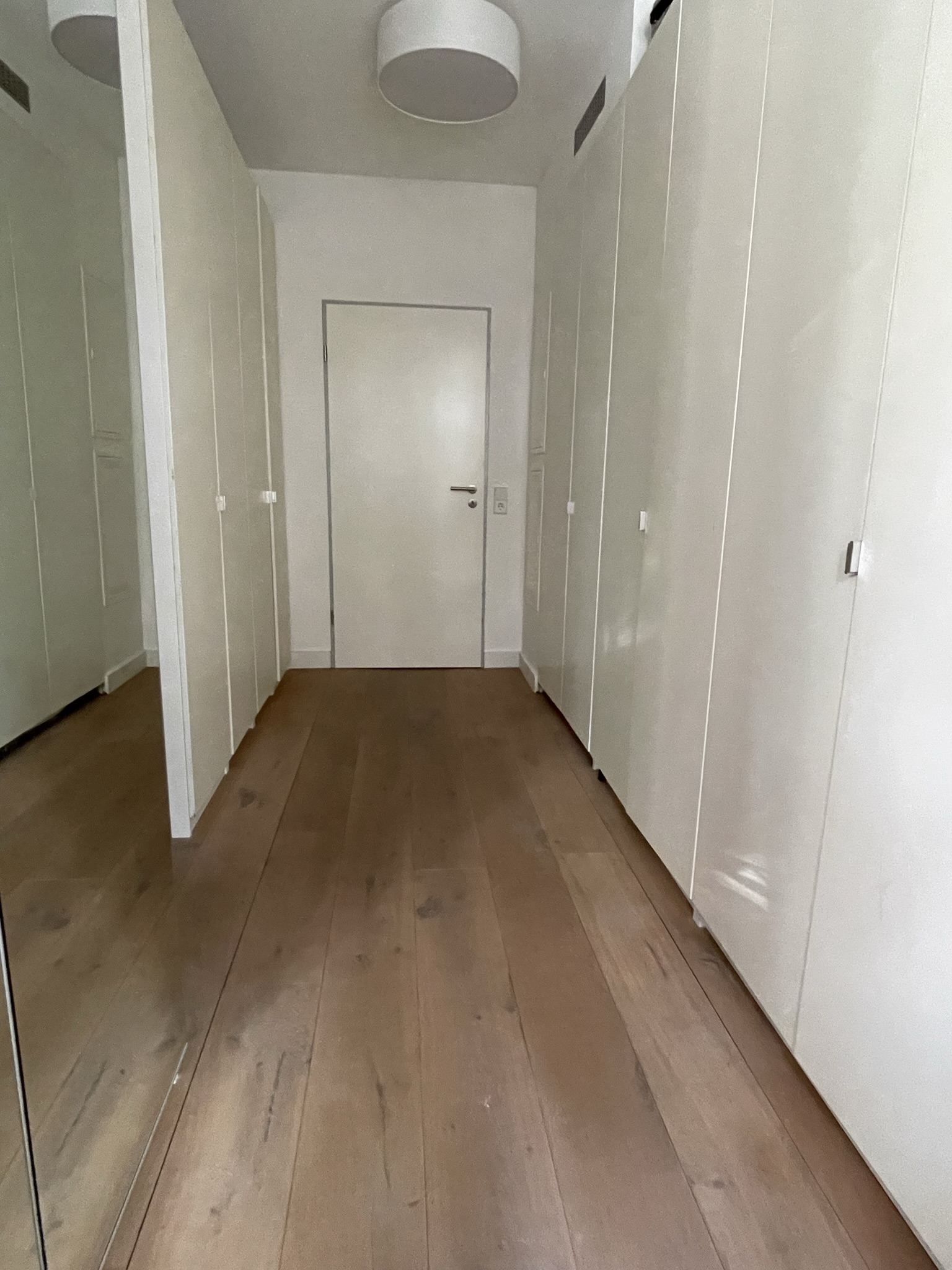 Schmaler Flur mit weißen Einbauschränken und Holzboden, Tür am Ende.