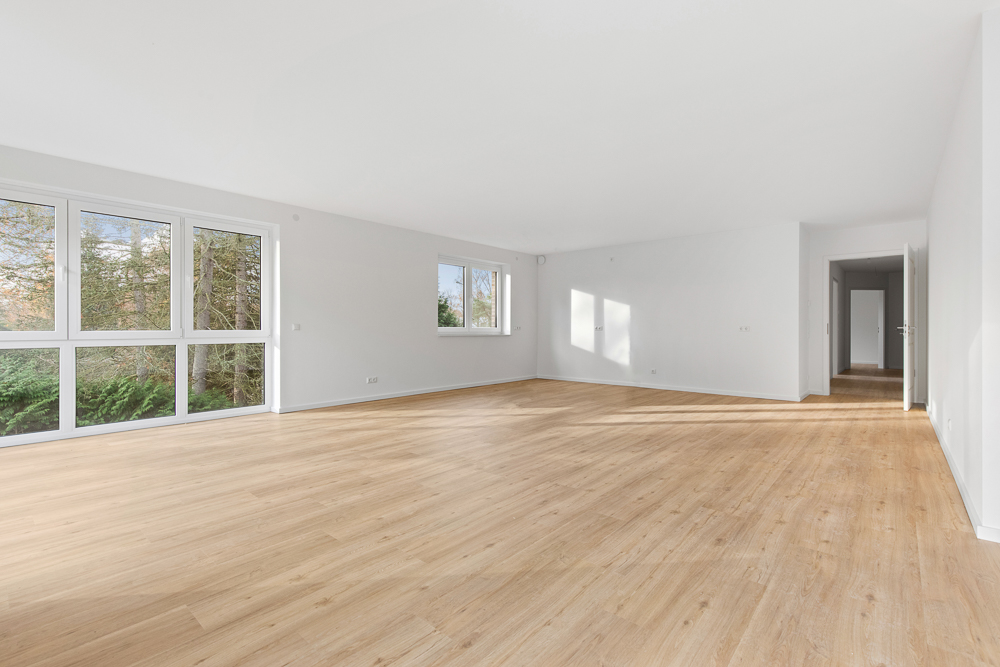 Helles, leeres Wohnzimmer mit großen Fenstern und hellem Holzboden.