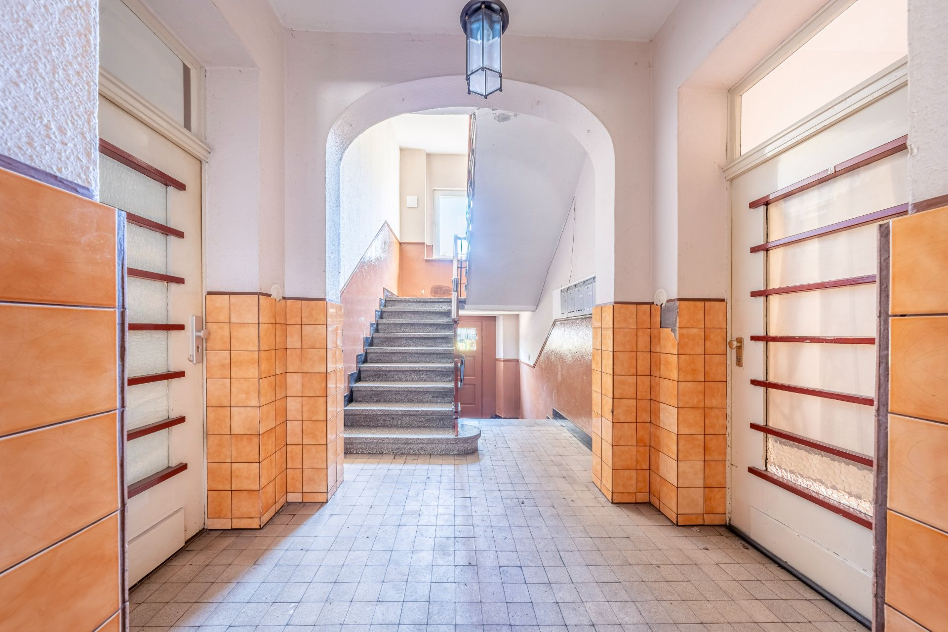 Flur eines Wohnhauses mit Treppe und gefliesten Wänden in Orange.