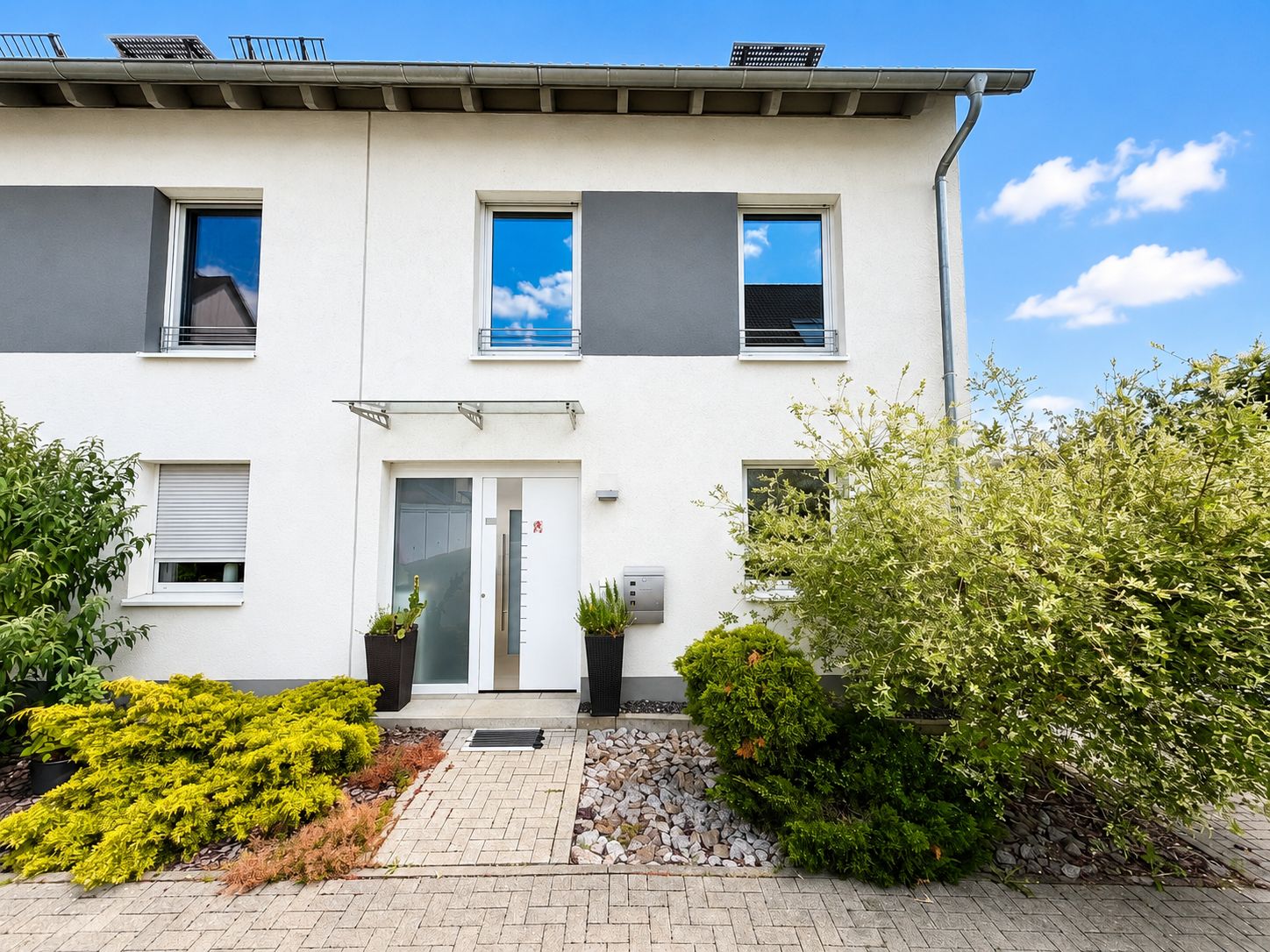 Vorderansicht eines modernen Reihenhauses mit Garten und zwei großen Fenstern.