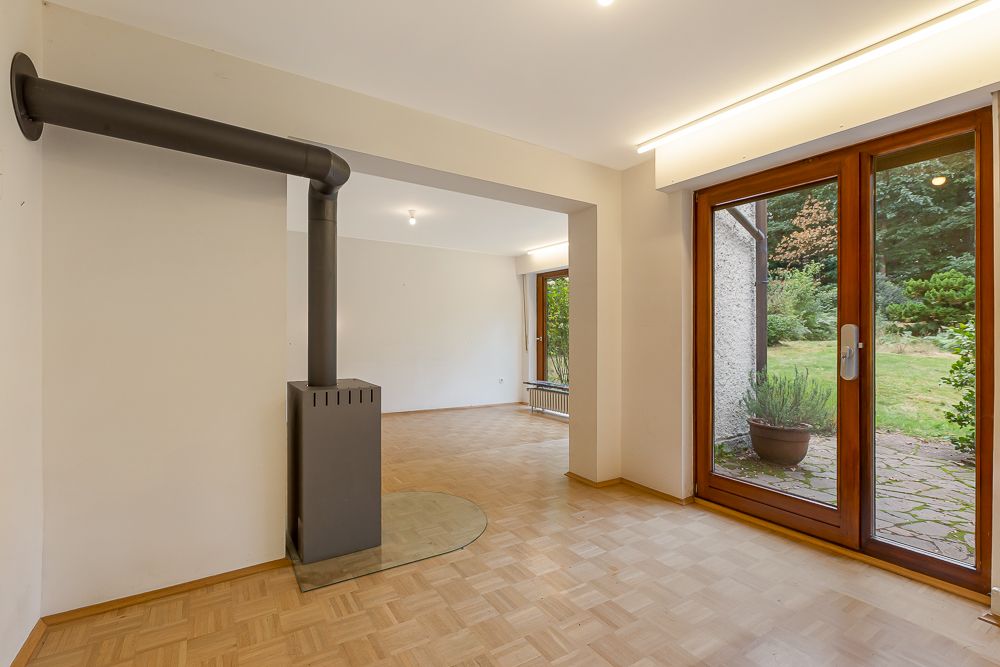 Helles Zimmer mit Parkettboden, Ofen und großer Glastür zum Garten.