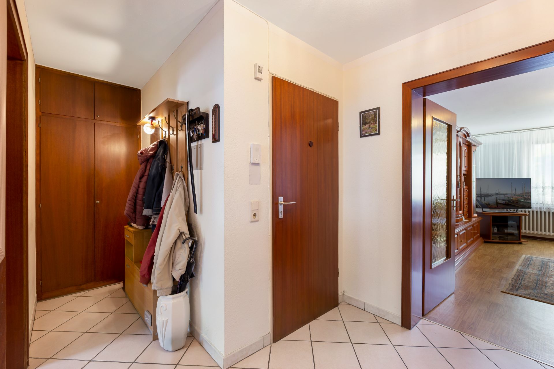 Eingangsbereich mit Garderobe, Holztüren und Blick ins Wohnzimmer mit Fernseher.
