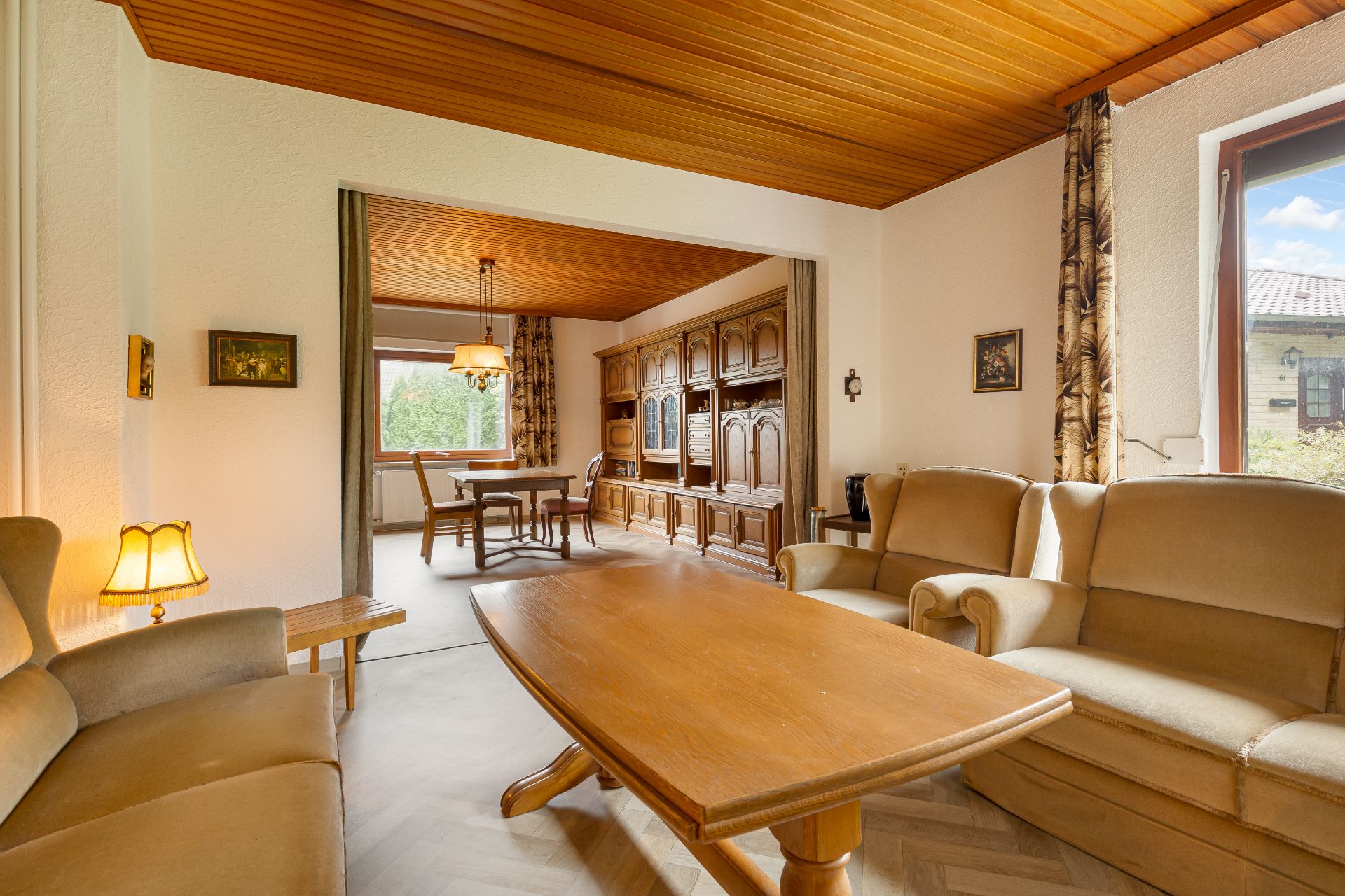 Wohnzimmer mit Holztisch, beigen Sofas und Blick auf Essbereich mit Schrankwand.