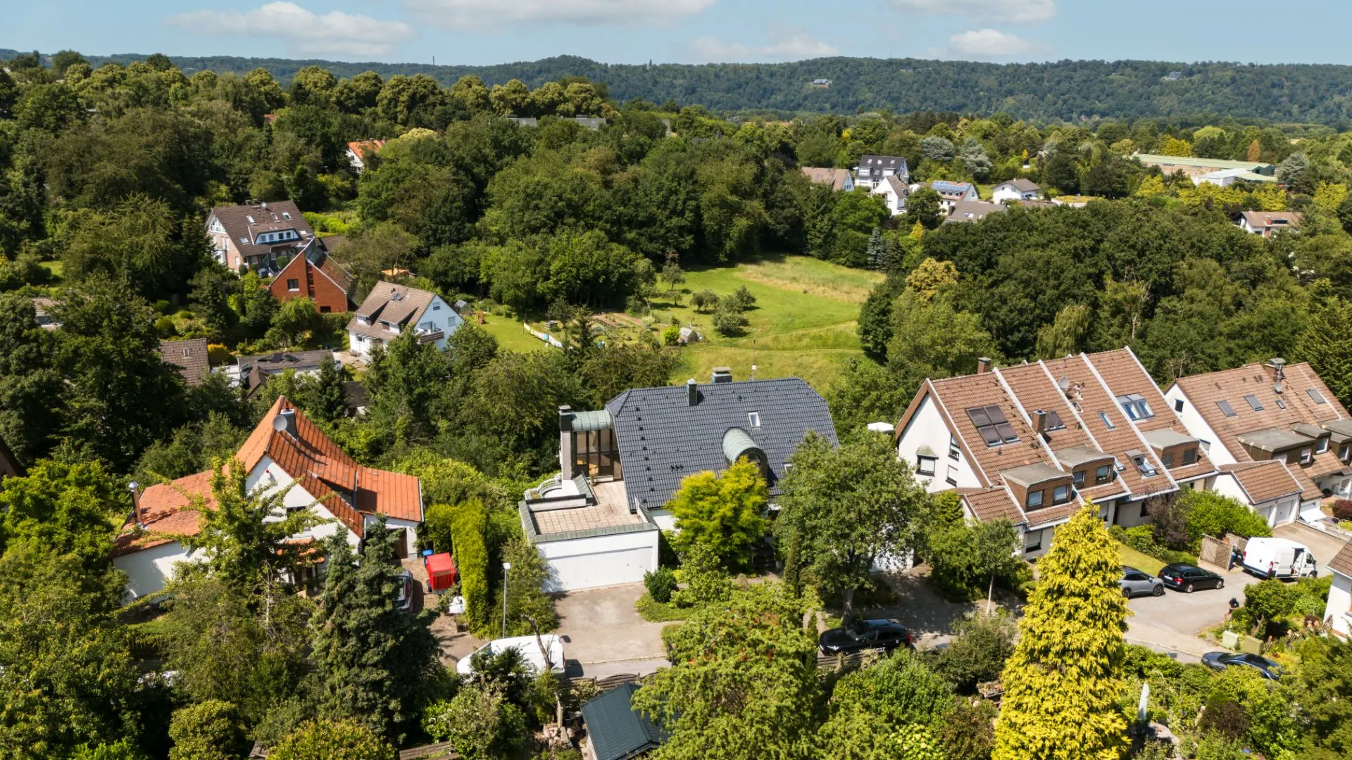 Luftaufnahme von Wohnhäusern mit Gärten und viel Grün in einer Vorortsiedlung.
