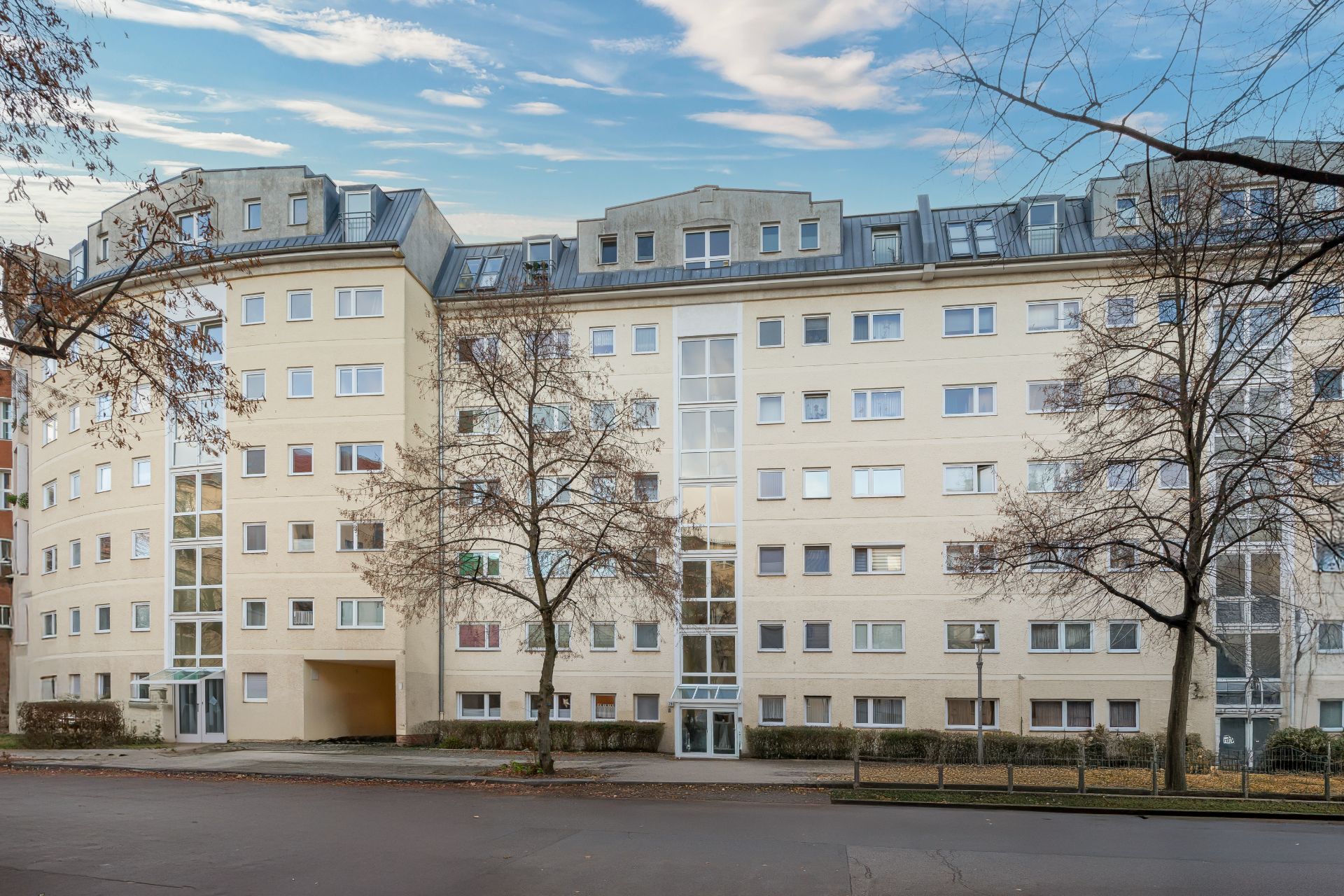Mehrstöckiges Wohngebäude mit vielen Fenstern und kahlen Bäumen davor.