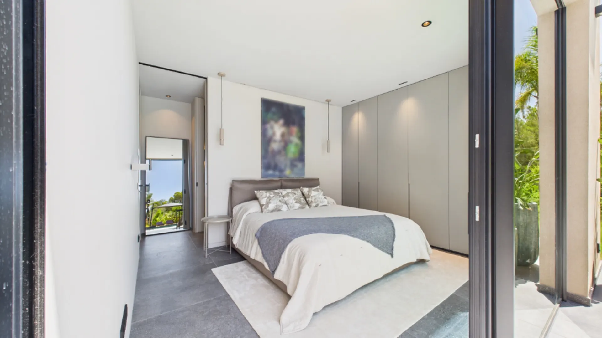 Modernes Schlafzimmer mit Doppelbett, grauem Schrank und großen Fenstern mit Ausblick ins Grüne.