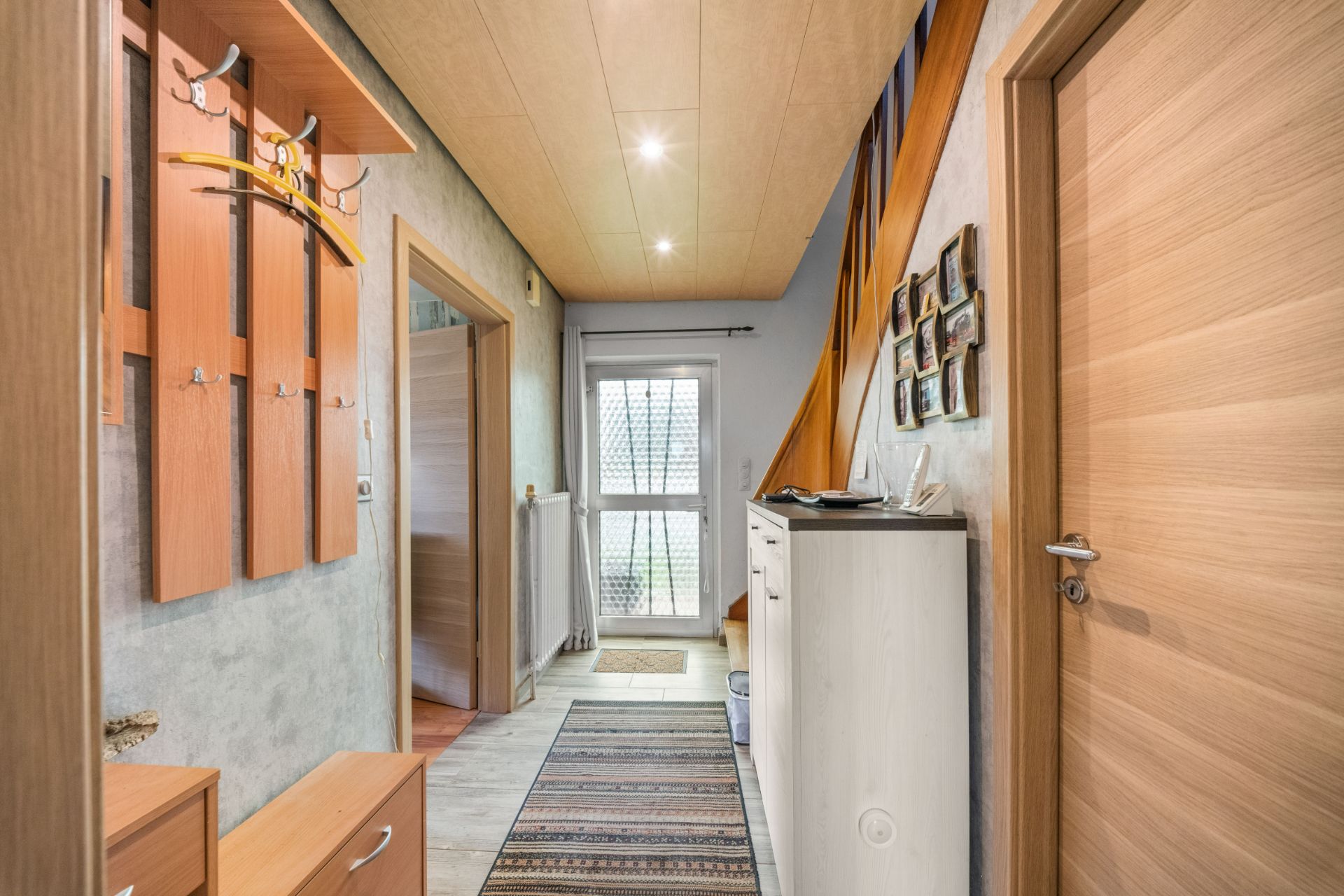 Heller Flur mit Garderobe, Kommode, Teppich und Türen, Blick auf eine verglaste Eingangstür.