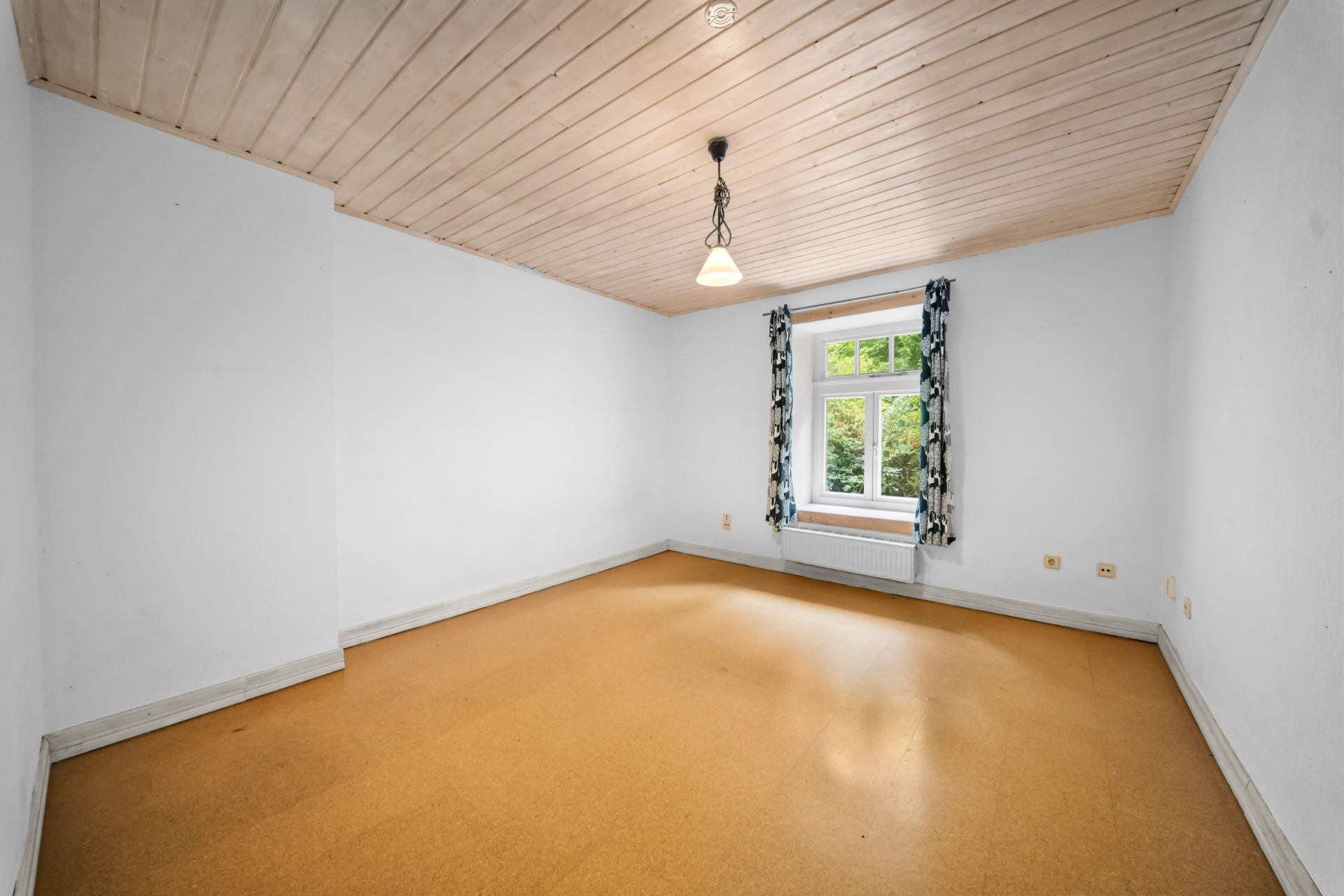 Leerer Raum mit Holzdecke, braunem Boden, Fenster und Vorhängen.