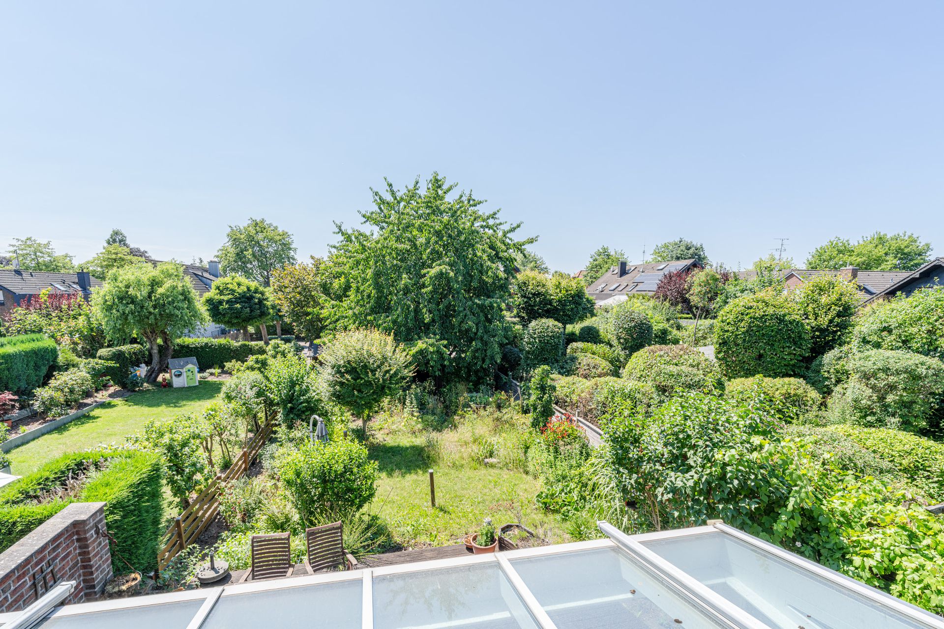 Großer, grüner Garten mit Bäumen, Sträuchern und Rasen, Blick von einer Terrasse.