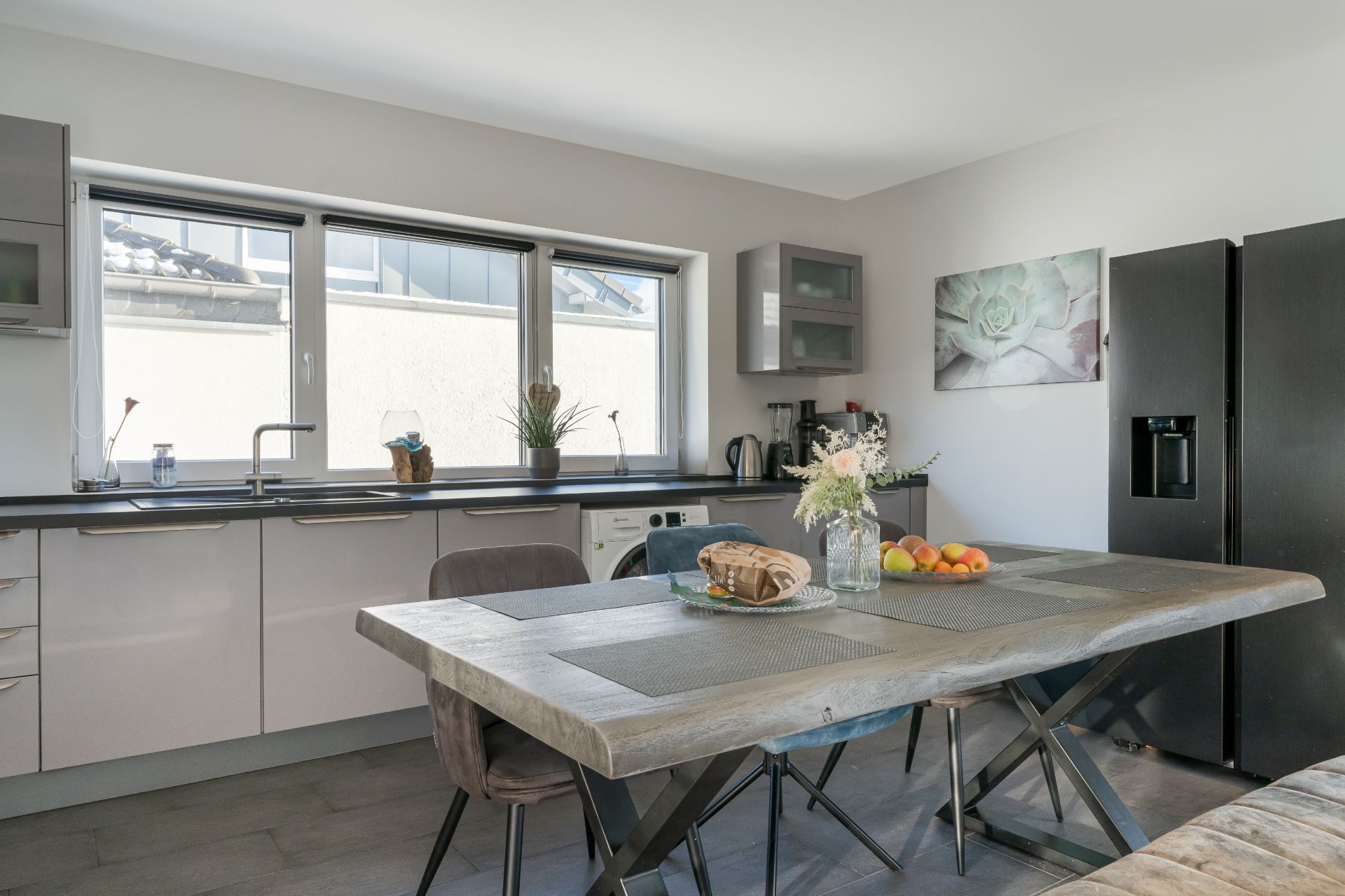 Moderne Küche mit großem Esstisch, Kühlschrank, Fenster und Dekorationen auf Tisch und Fensterbank.