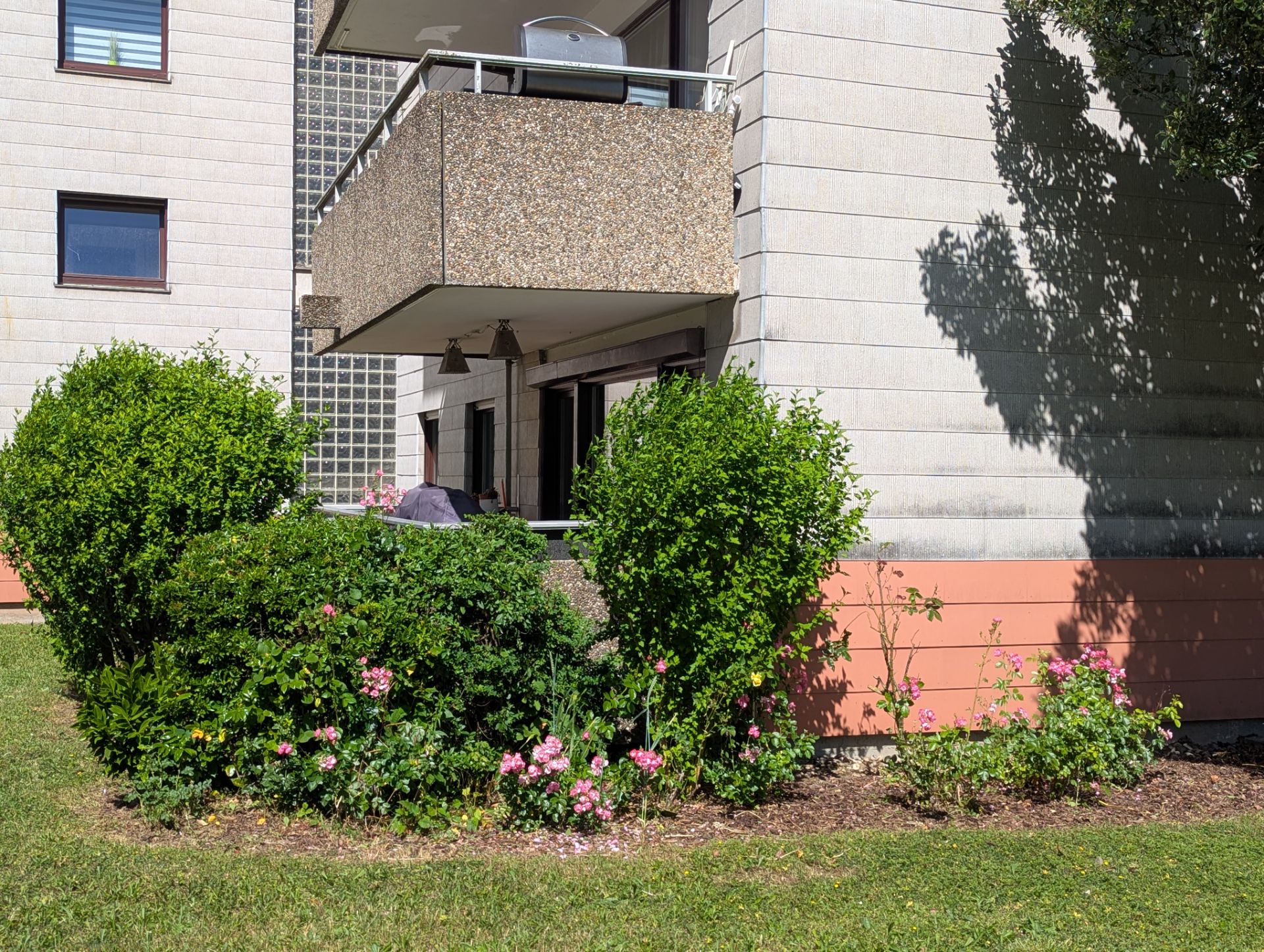 Wohnhaus mit Balkon, davor blühende Sträucher und Blumen im Garten.