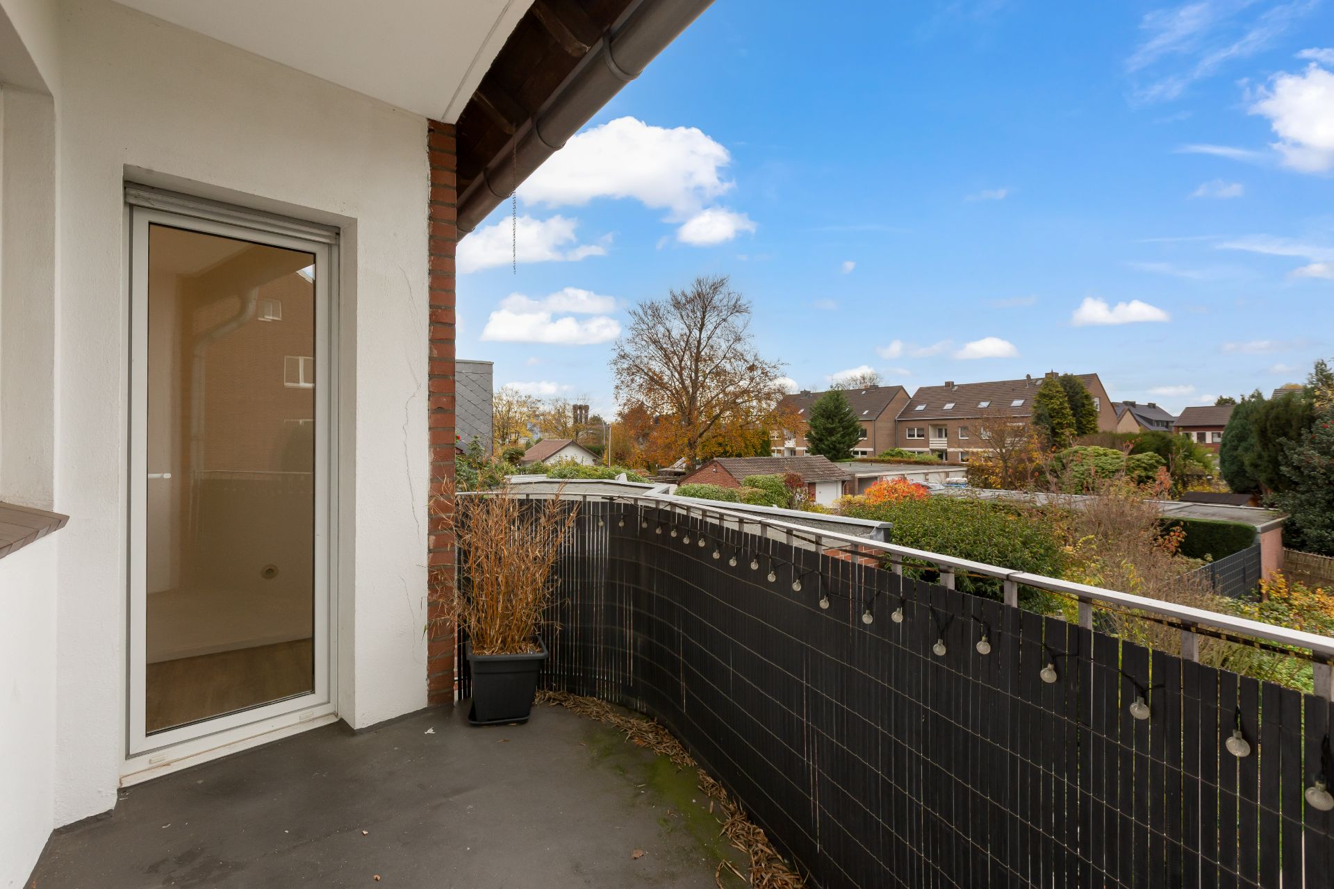 Balkon mit Blick auf Nachbarhäuser und Bäume, Glas­tür und Blumenkasten sichtbar.