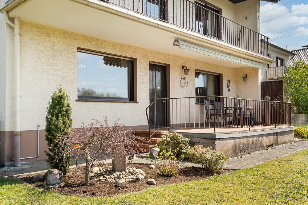 Terrasse eines Wohnhauses mit Garten und Sitzbereich, davor Blumenbeet.