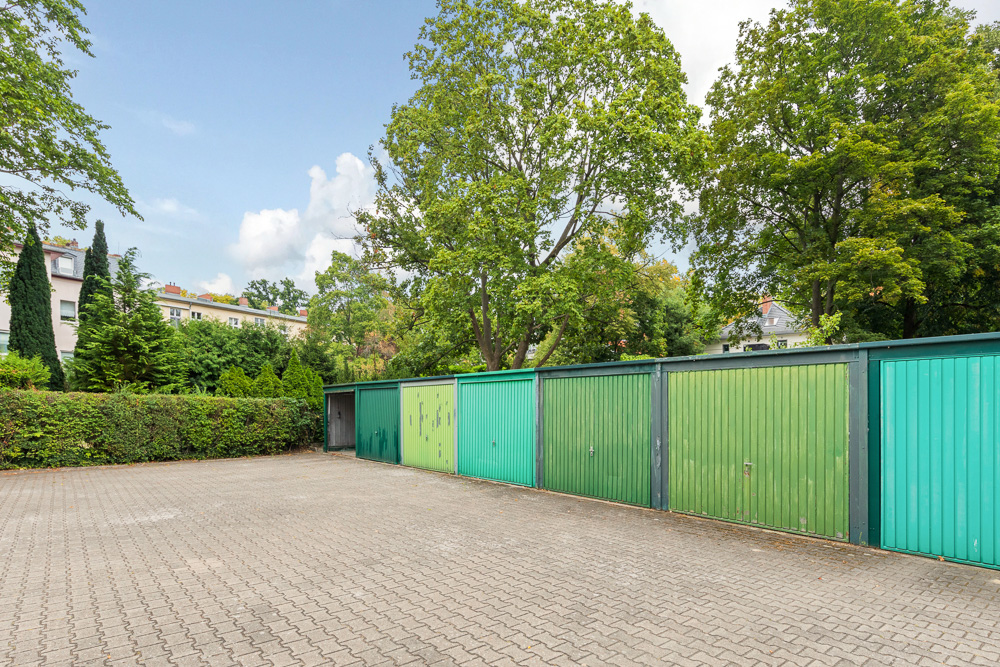 Reihe von grünen Garagentoren mit Bäumen und Wohnhäusern im Hintergrund.
