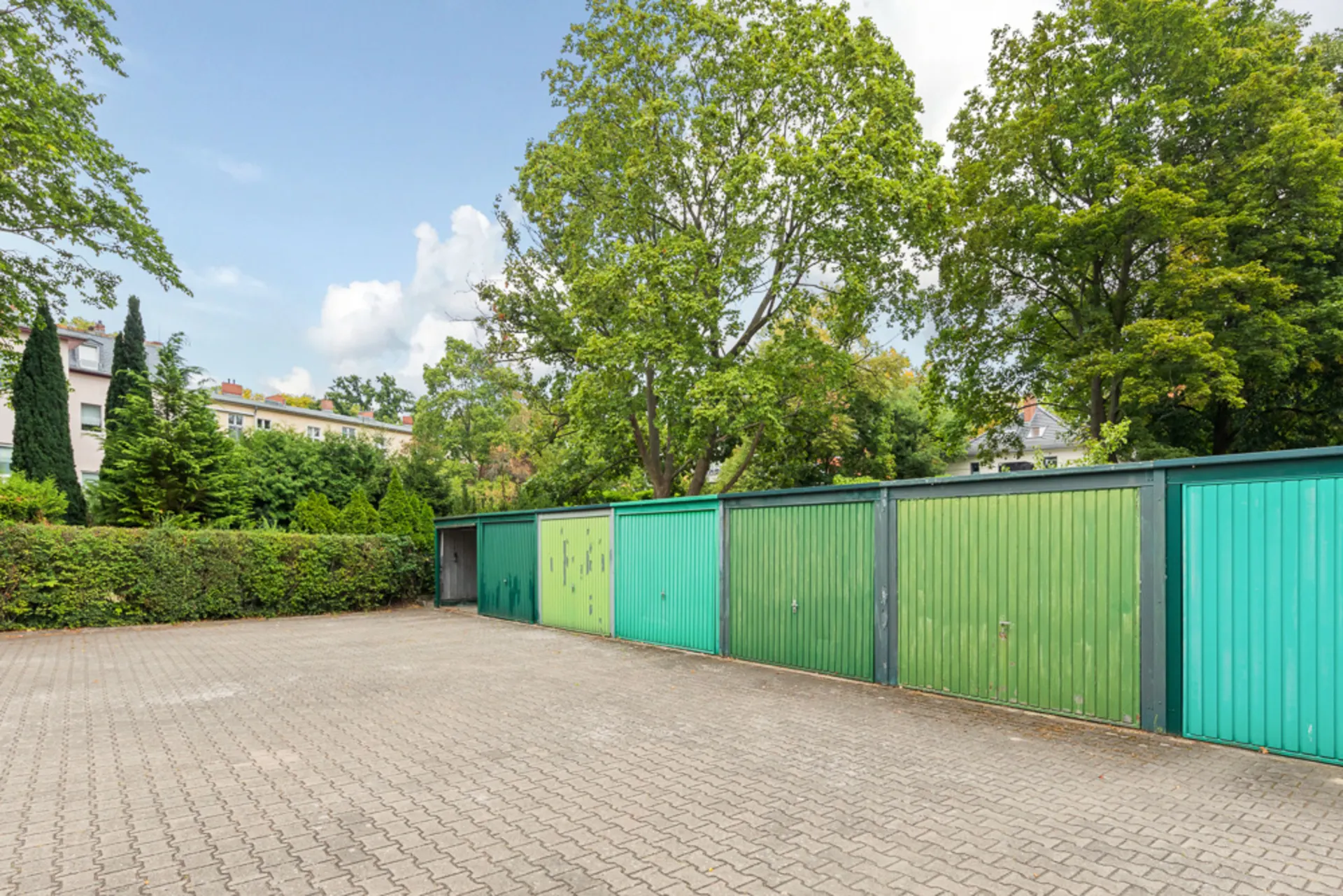 Reihe von grünen Garagentoren mit Bäumen und Wohnhäusern im Hintergrund.