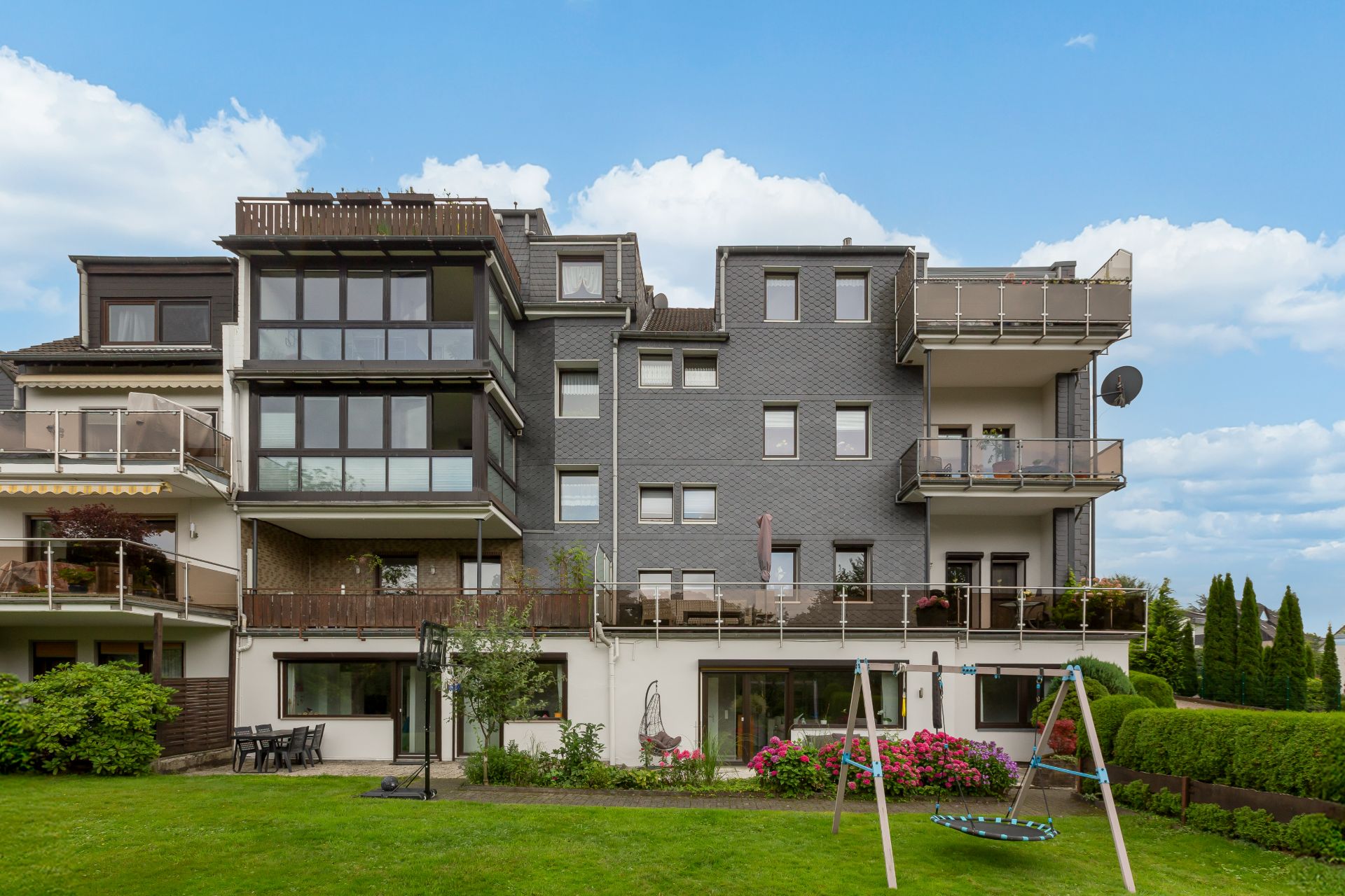 Mehrfamilienhaus mit Balkonen, Garten und Schaukel im Vordergrund.