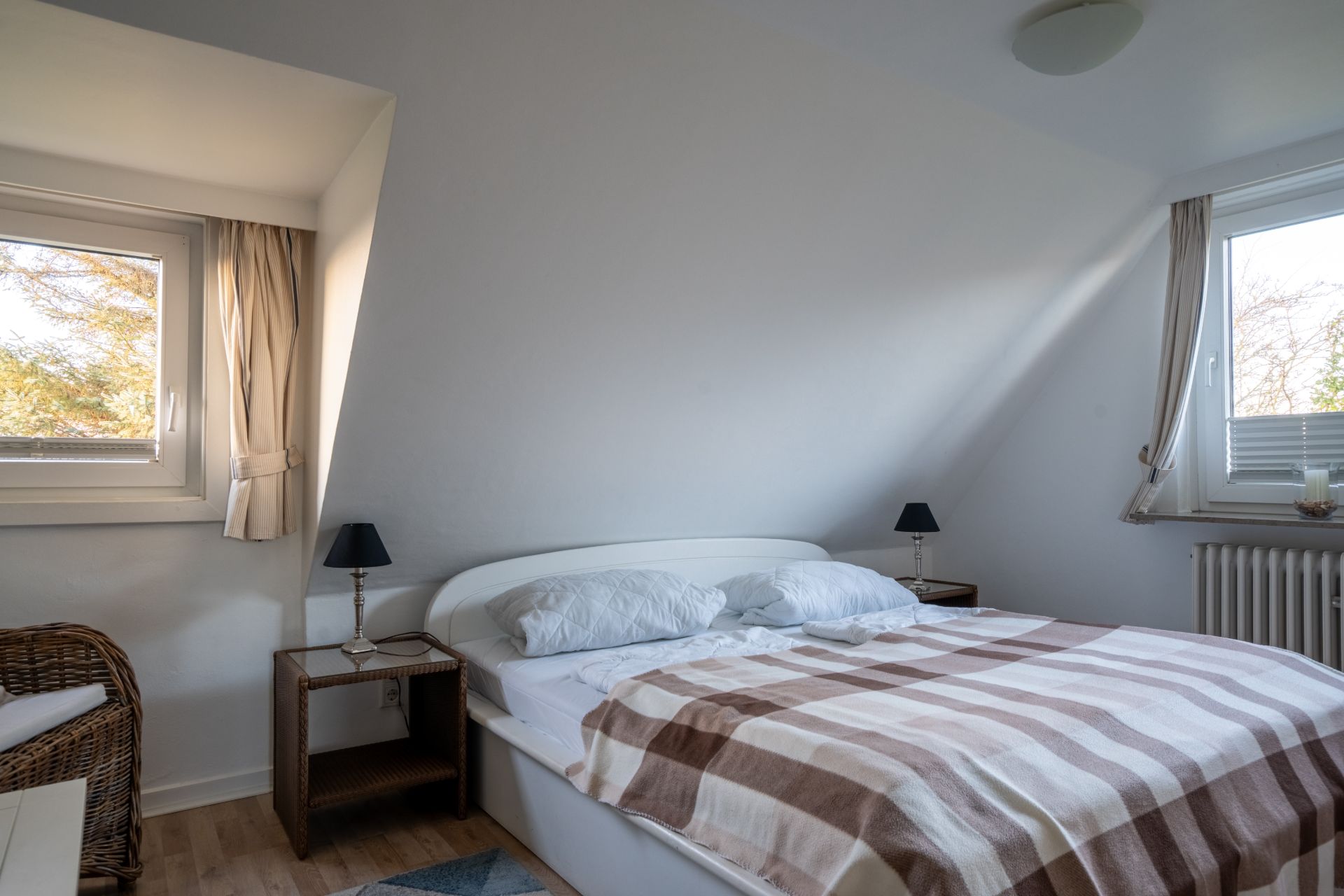 Helles Schlafzimmer mit Doppelbett, zwei Fenstern, Nachttischen und Lampen.