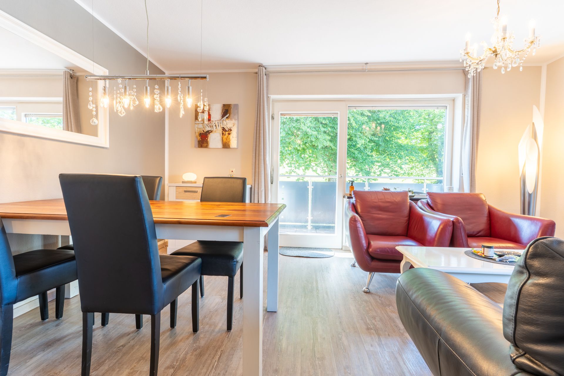 Helles Wohnzimmer mit Esstisch, schwarzen Stühlen und roten Sesseln vor großen Fenstern.