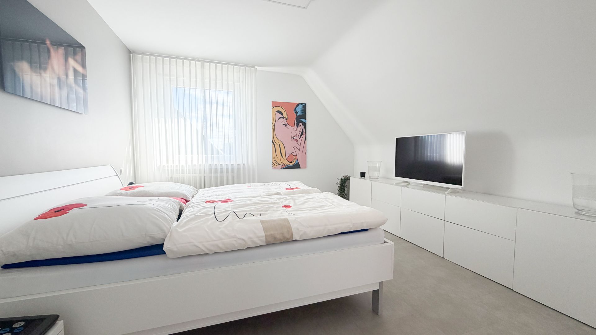 Helles Schlafzimmer mit großem Bett, Kommode, Fernseher und zwei Wandbildern.