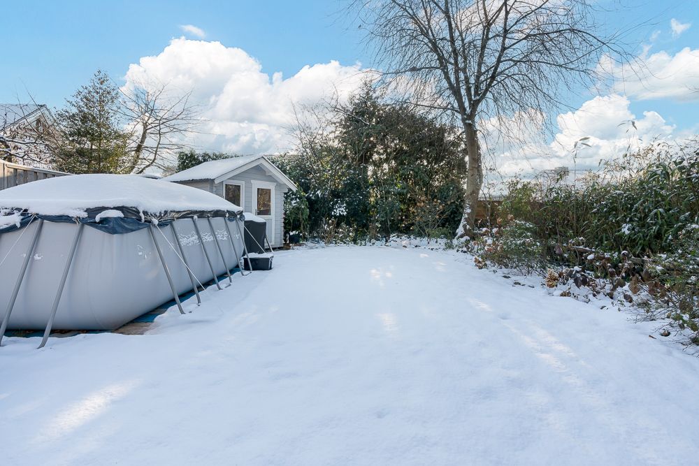 Schneebedeckter Garten mit aufgestelltem Pool, Baum und kleinem Gartenhaus.