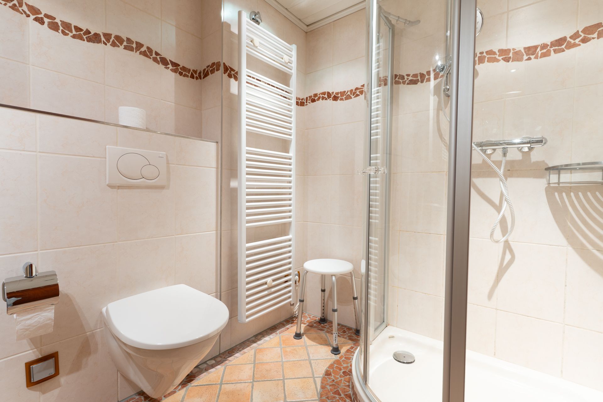 Modernes Badezimmer mit Dusche, Wandtoilette, Handtuchheizkörper und Hocker.
