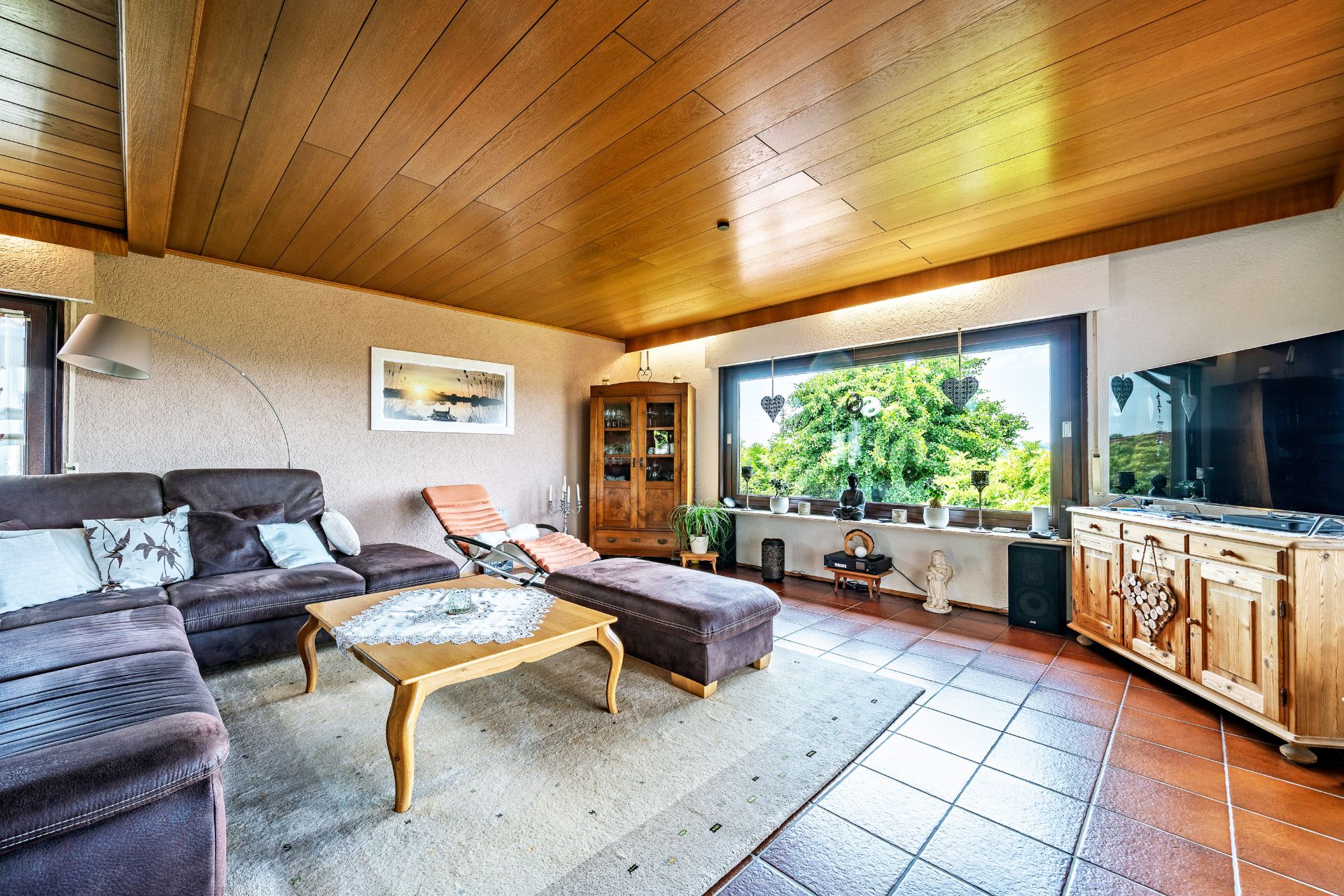 Wohnzimmer mit Ecksofa, Couchtisch, Fernseher, großem Fenster und Holzmöbeln.