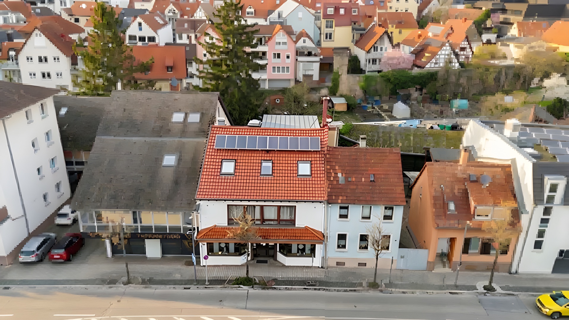 Mehrstöckiges Wohnhaus mit roten Dachziegeln und Solarpanelen, umgeben von weiteren Gebäuden.