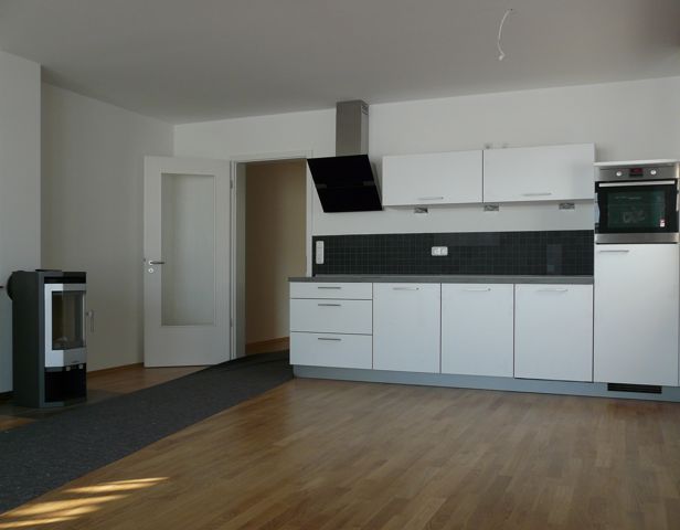 Moderne Einbauküche mit weißen Schränken, Holzfußboden und offener Tür zu einem Flur.