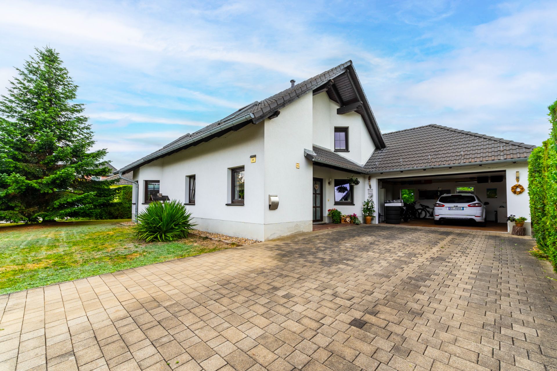 Modernes Einfamilienhaus mit grauem Dach, Auffahrt und gepflegtem Garten.