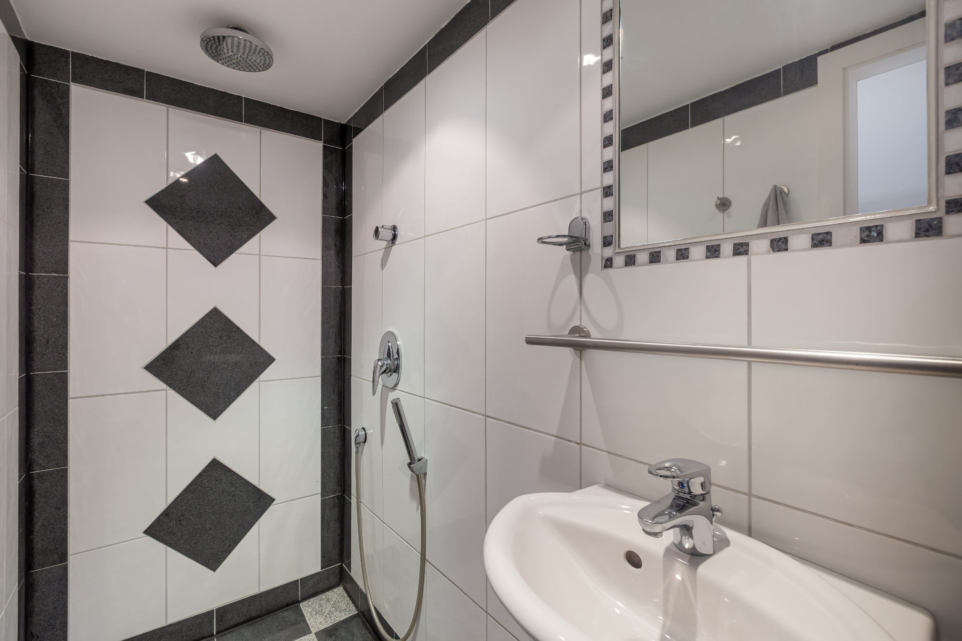 Modernes Badezimmer mit Dusche, weißen Fliesen, Waschbecken und Wandspiegel.