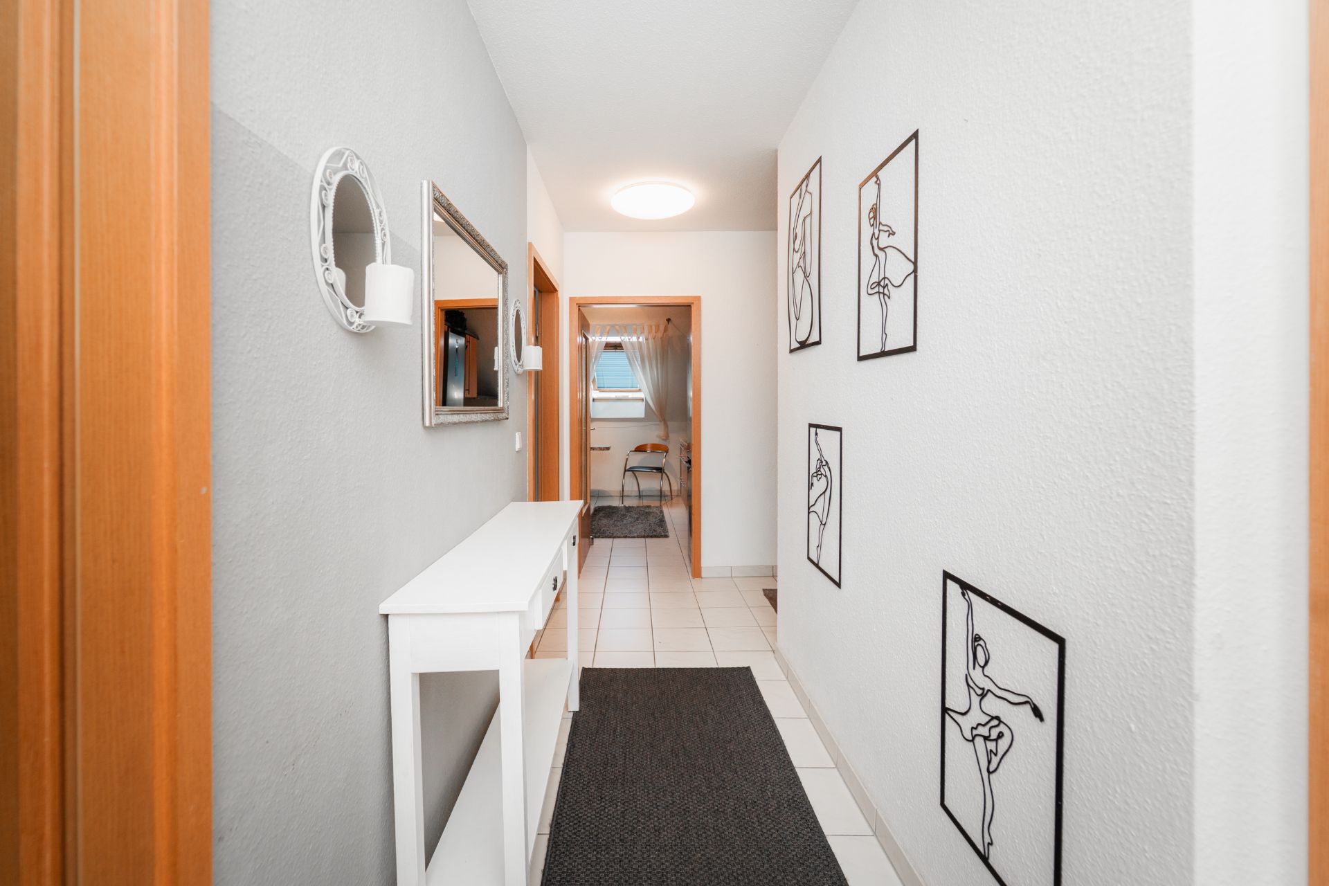 Heller Flur mit weißem Sideboard, Spiegel und linearen Kunstdrucken an der Wand.