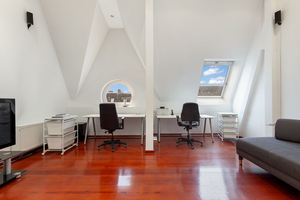 Helles Arbeitszimmer mit zwei Schreibtischen, Stühlen, Sofa und schrägen Decken unter dem Dachfenster.