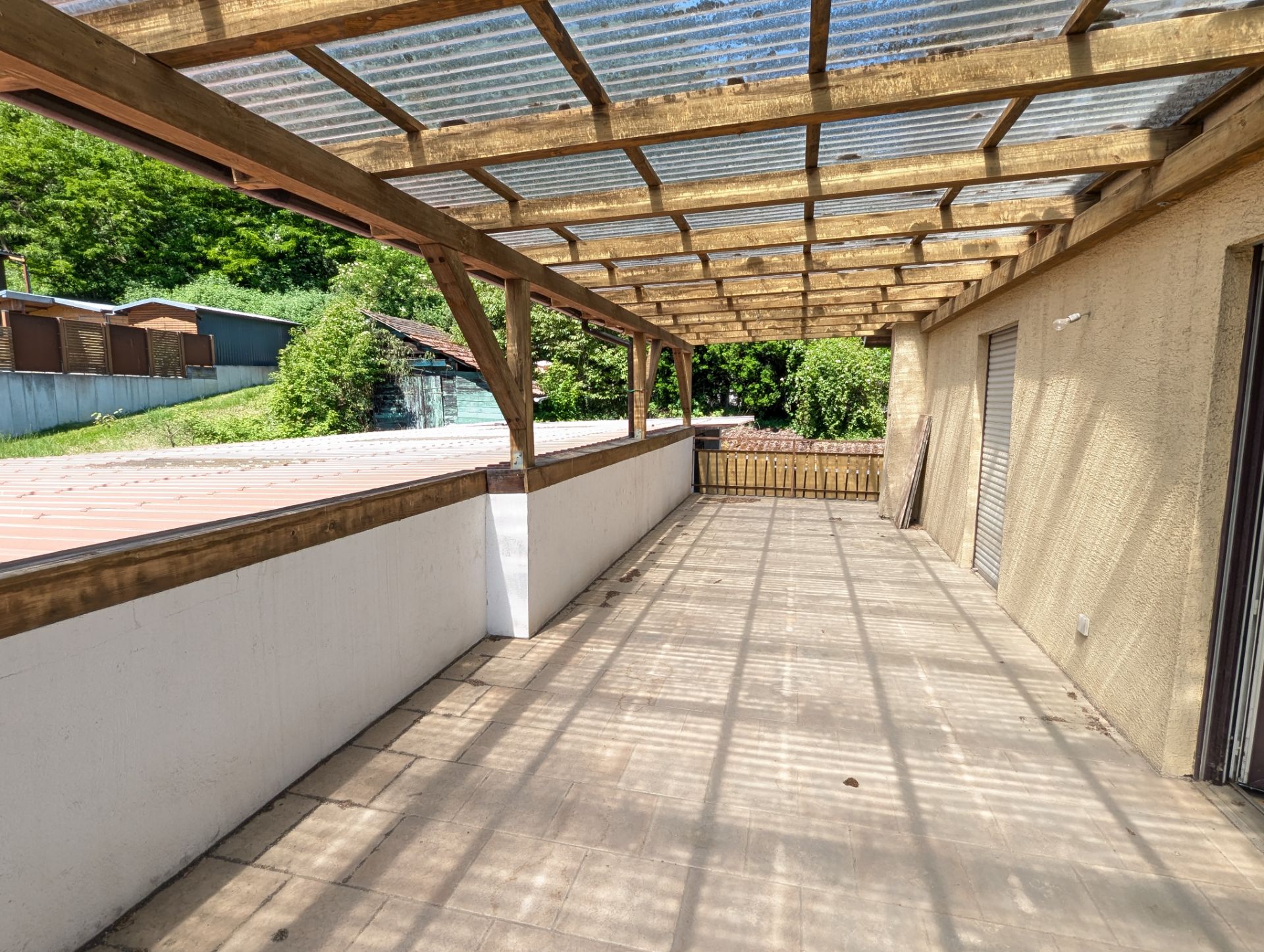 Überdachte Terrasse mit Holzbalken und Blick ins Grüne an einem Wohnhaus.