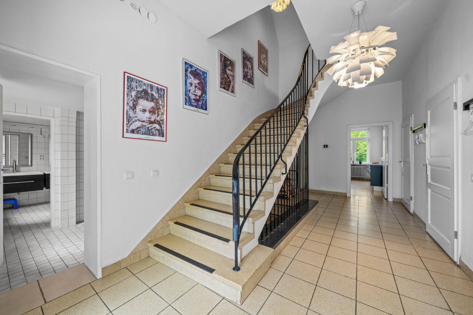Heller Flur mit Treppe, modernen Lampen und Bildern an der Wand.